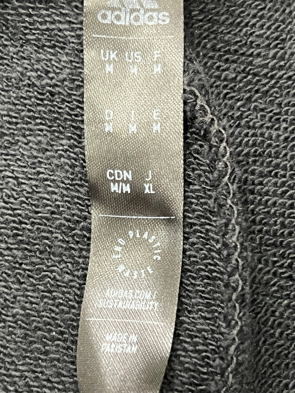 Close-up of Adidas label inside the black tracksuit bottoms showing size and sustainability print