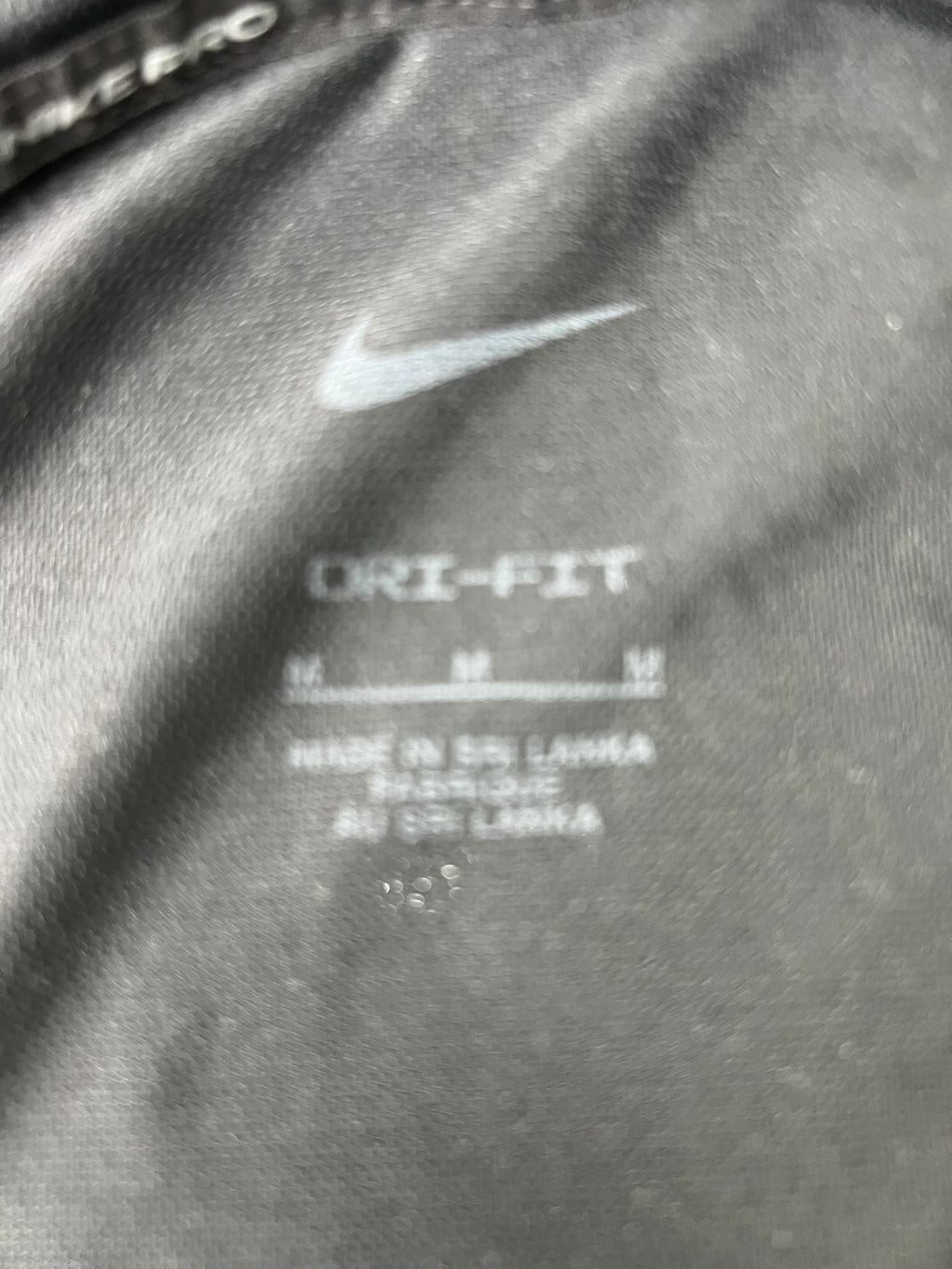 Close-up of inside label of black Nike Dri-FIT t-shirt showing size and care information