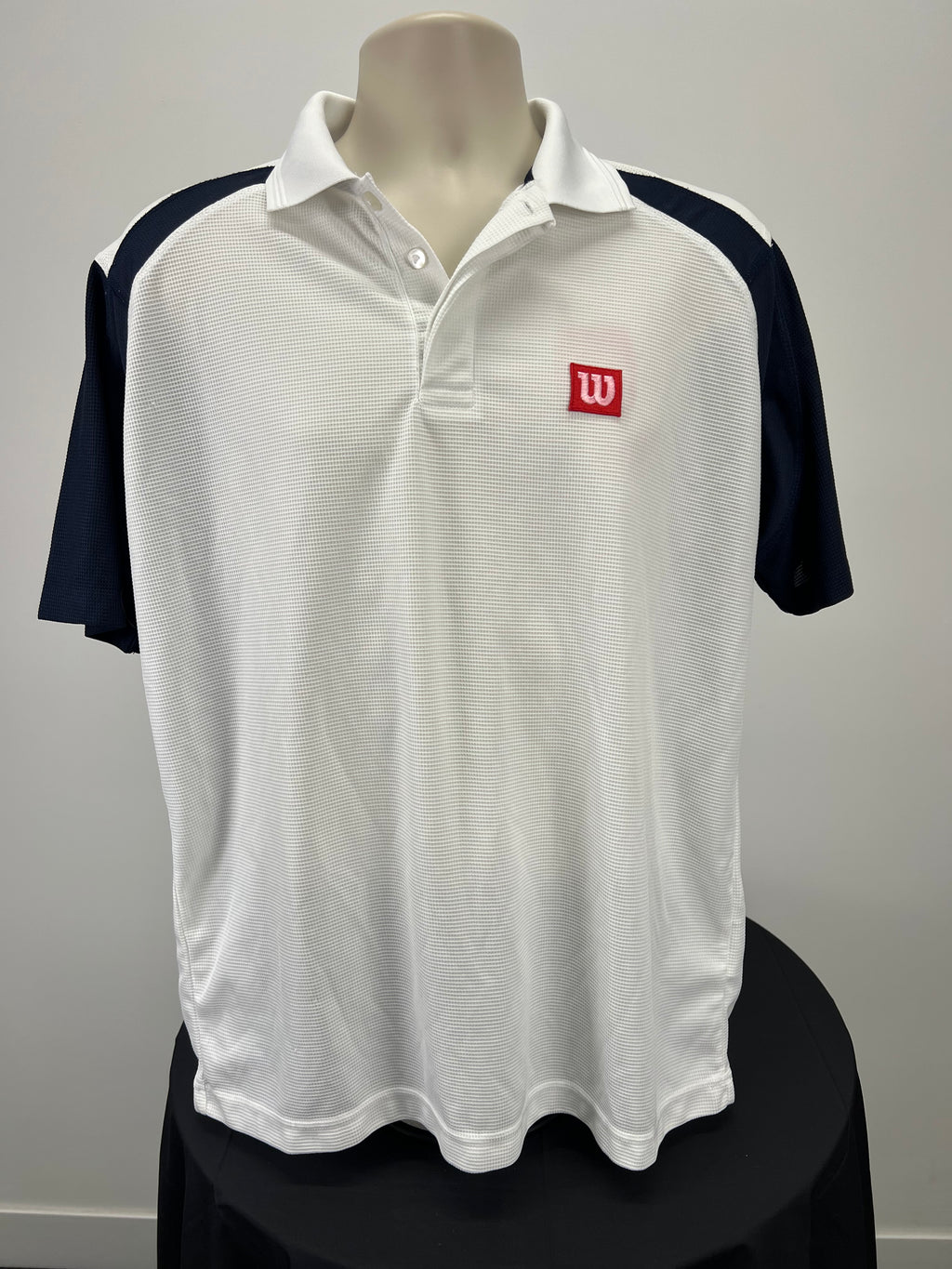 Front view of men's Wilson polo shirt in white with navy sleeves featuring a red embroidered Wilson logo on the chest
