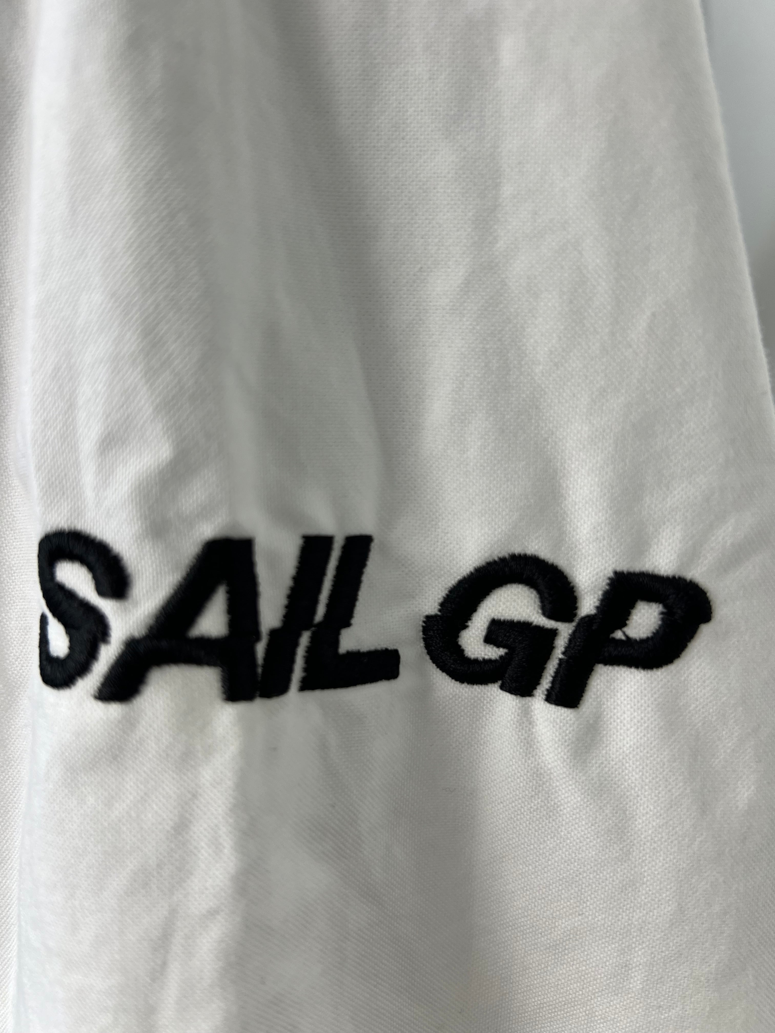 Close-up of embroidered 'SAIL GP' logo on the sleeve of the white shirt