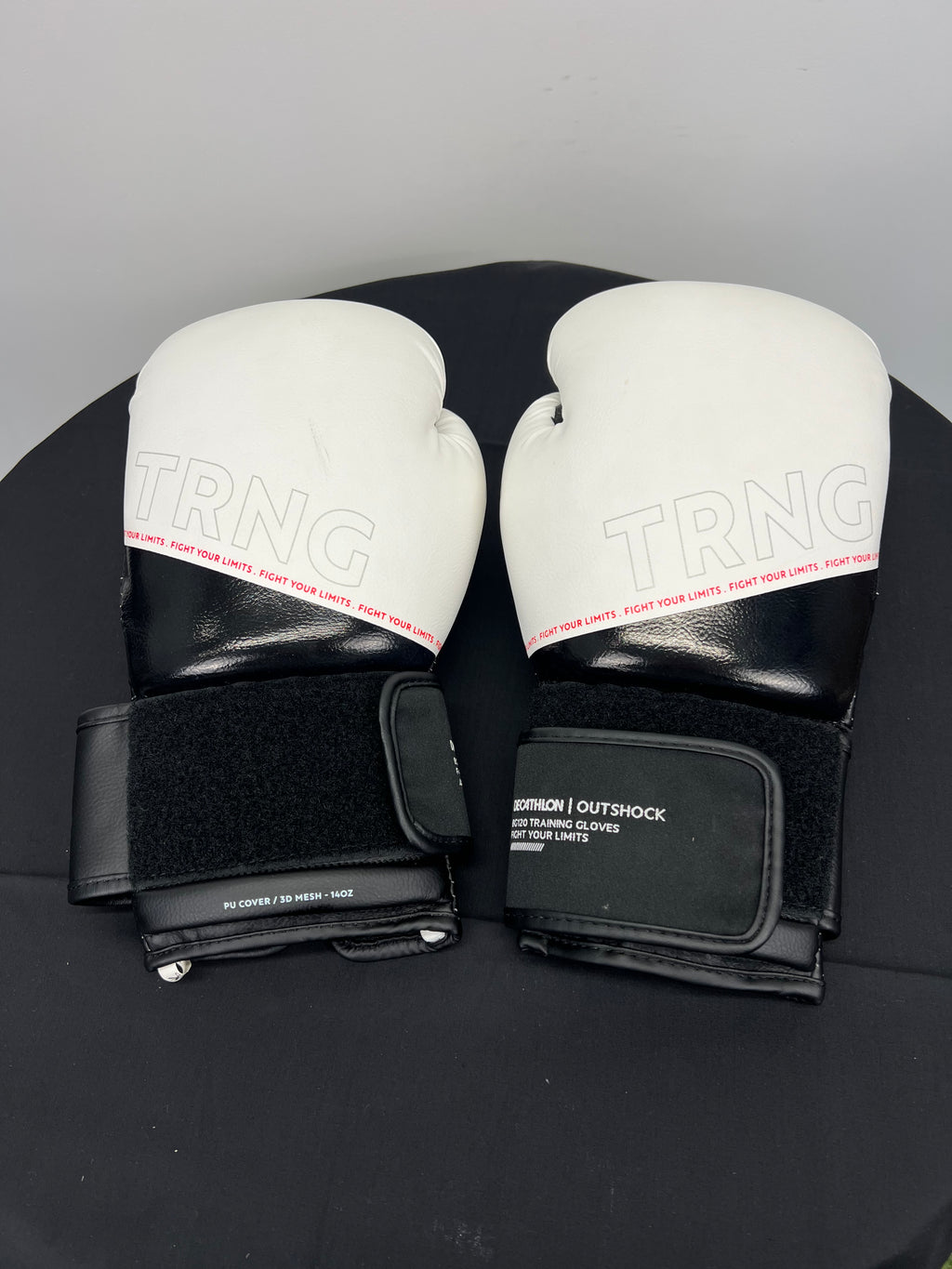 Pair of TRNG Outshock boxing gloves with white top and black lower section on black surface