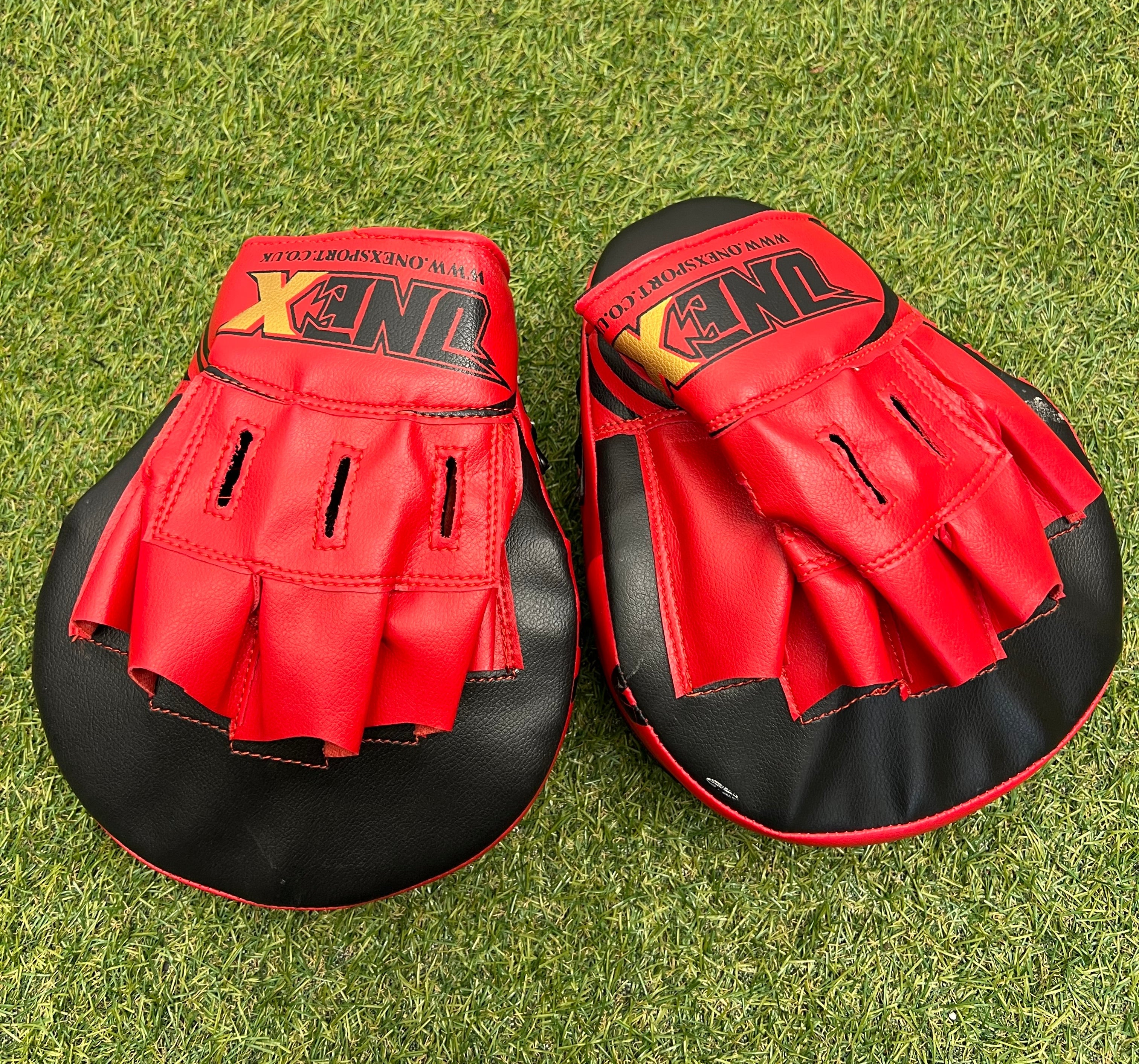 Pair of red and black Onex Sport MMA sparring pads with finger slots placed on grass