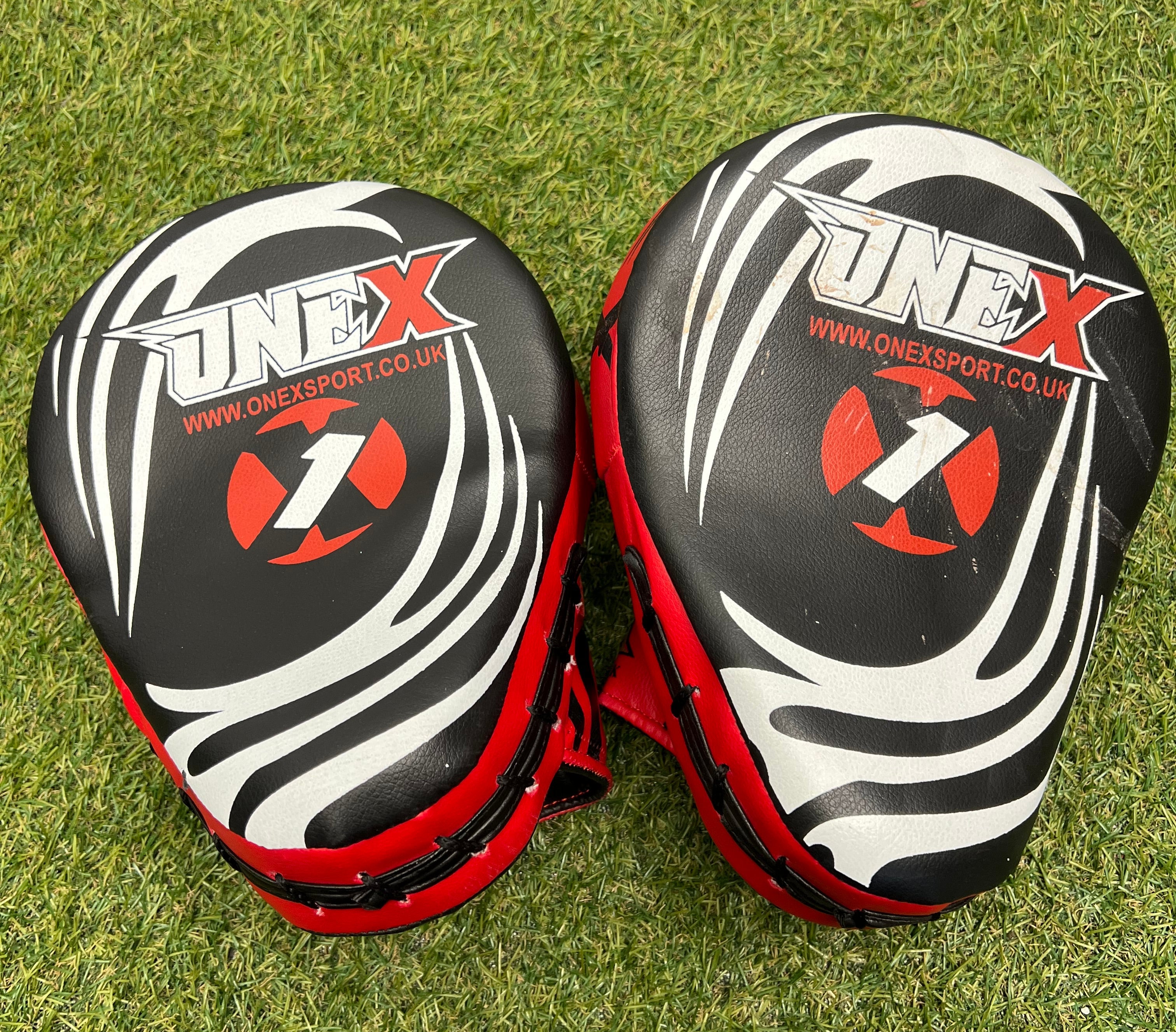 Back view of Onex Sport MMA sparring pads showing black surface with white and red graphics on grass