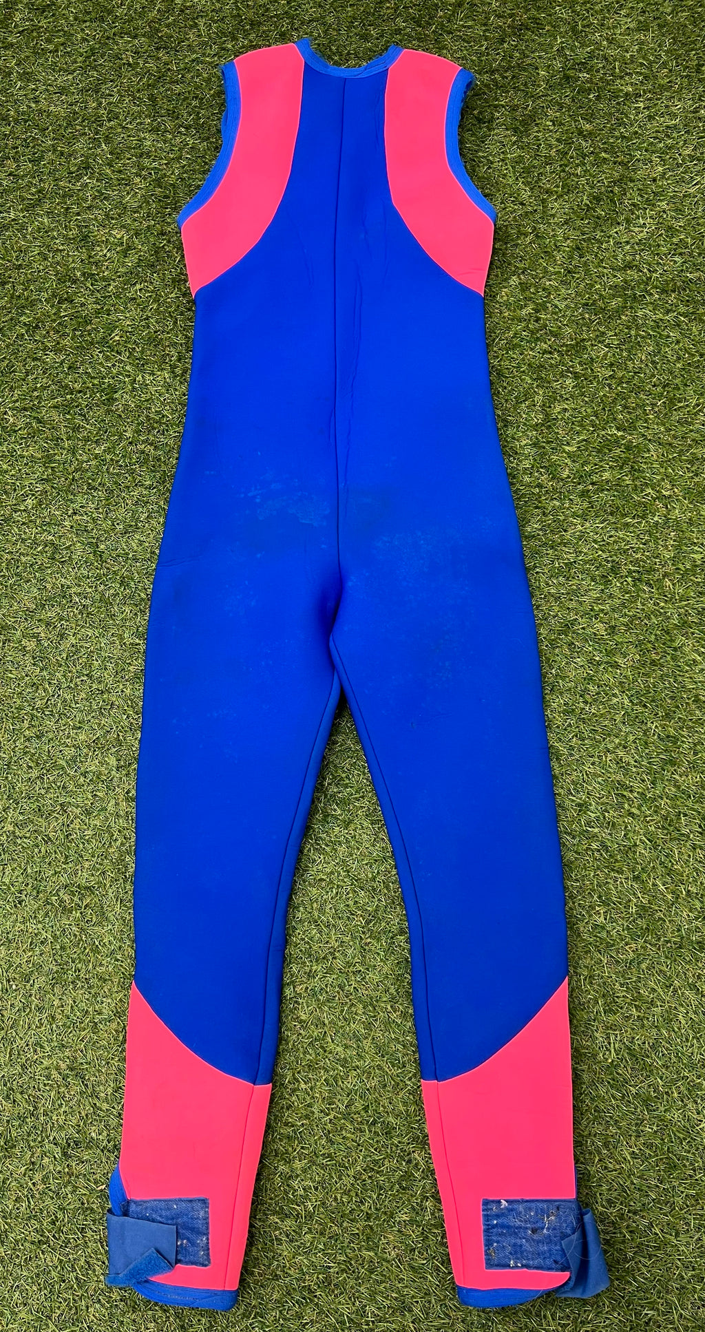 Back view of blue sleeveless wetsuit with bright pink panels on shoulders and lower legs showing Velcro ankle straps