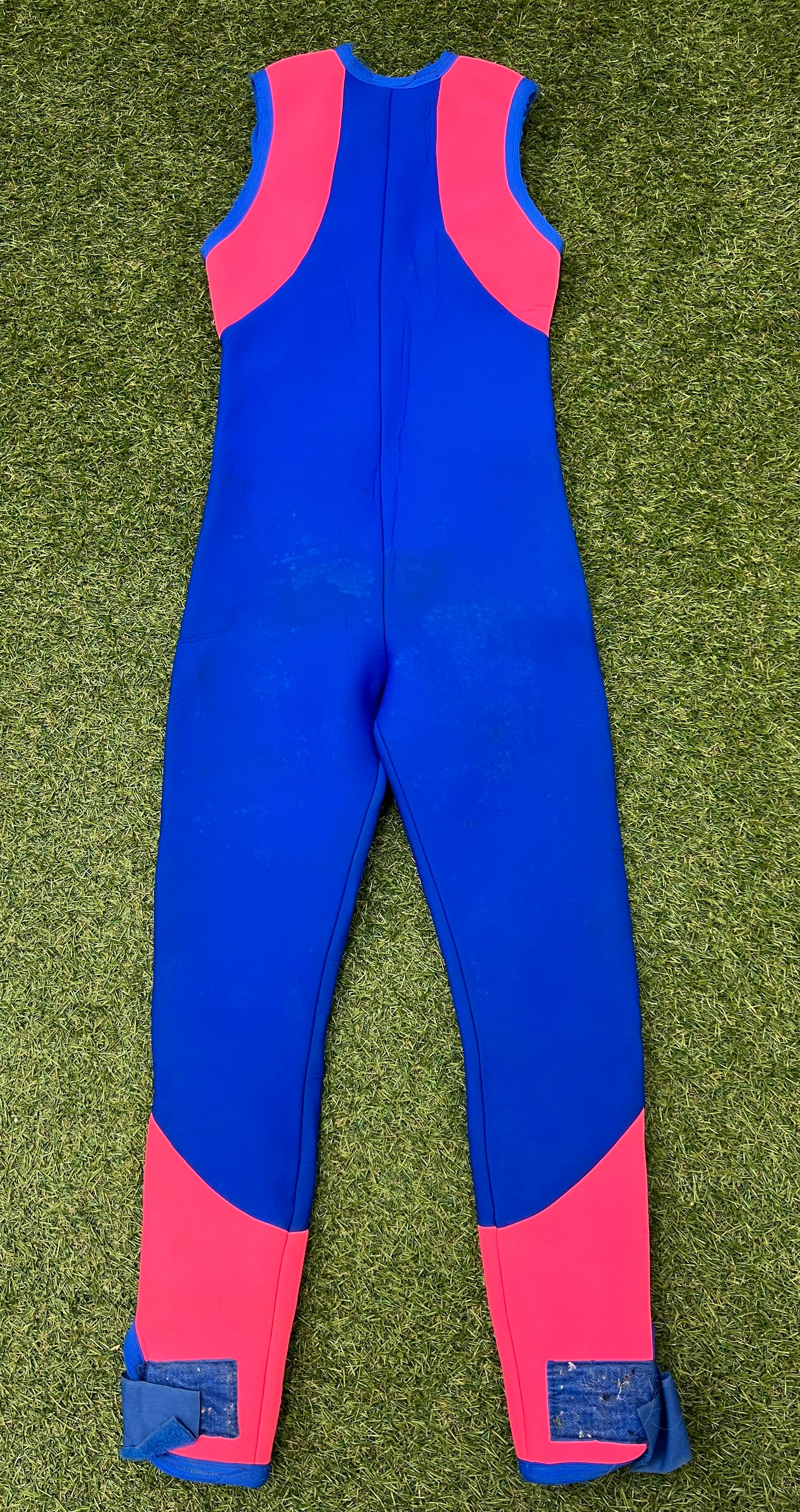Back view of blue sleeveless wetsuit with bright pink panels on shoulders and lower legs showing Velcro ankle straps