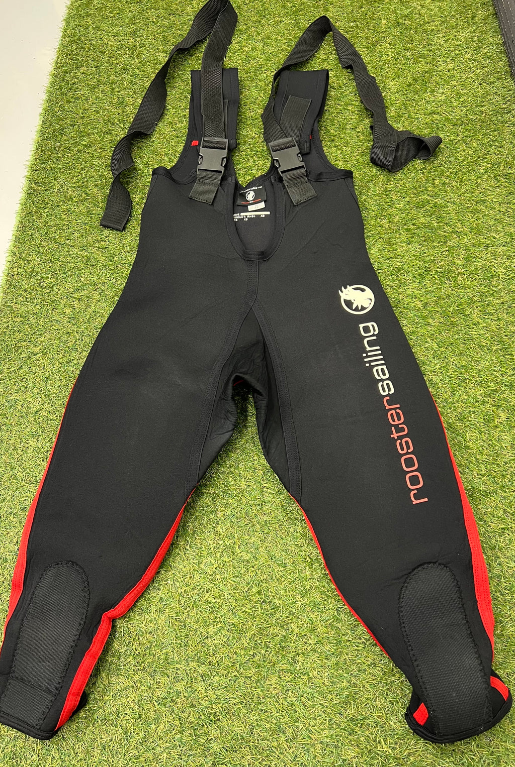 Front view of black and red Rooster sailing neoprene bib trousers laid flat showing adjustable shoulder straps