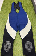 Front view of sleeveless blue, grey, and black neoprene wetsuit bib trousers with cross-back straps and padded knees, laid flat on grass