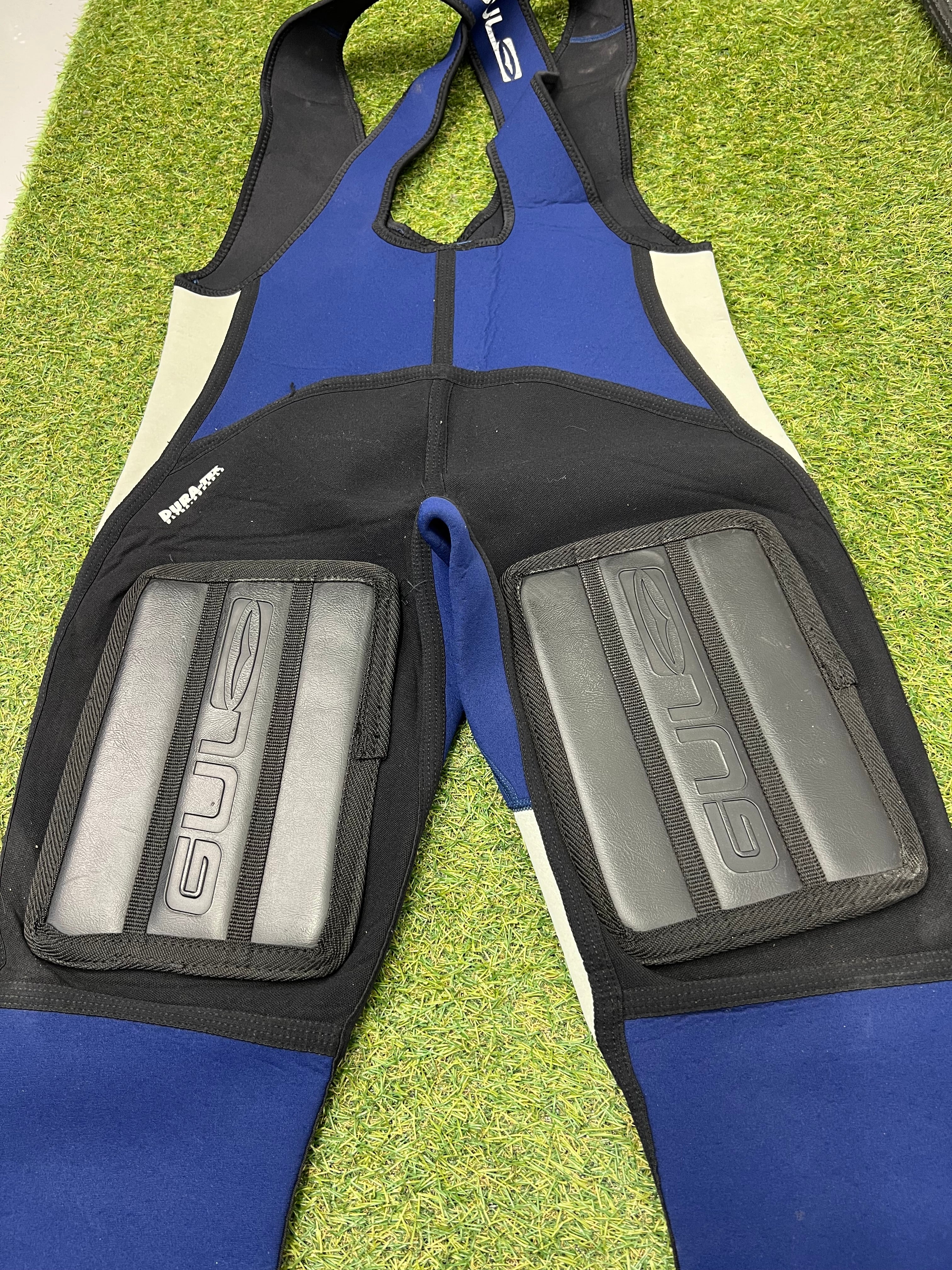 Detailed rear view of knee padding with Gul logos on black neoprene sections of sleeveless wetsuit bib trousers