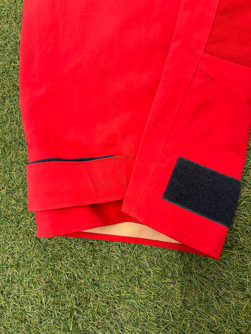 Close-up of ankle velcro fastening on red trousers with inner waterproof lining visible.