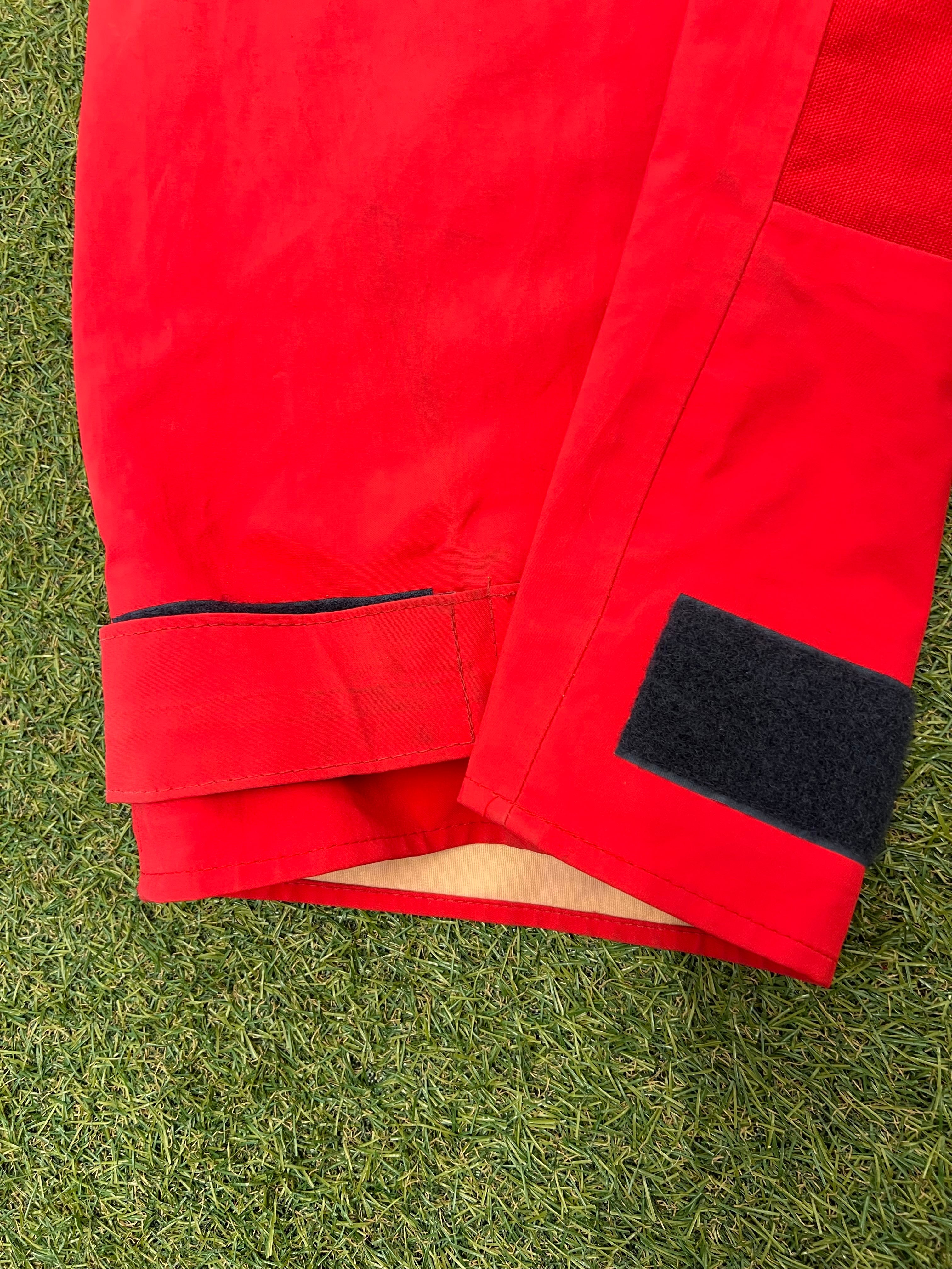 Close-up of ankle velcro fastening on red trousers with inner waterproof lining visible.