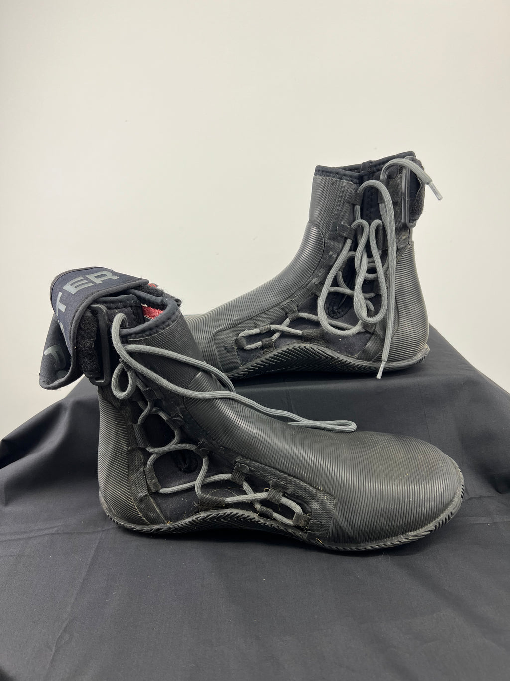 Pair of black Rooster Pro laced ankle strap boots with grey laces on black cloth background