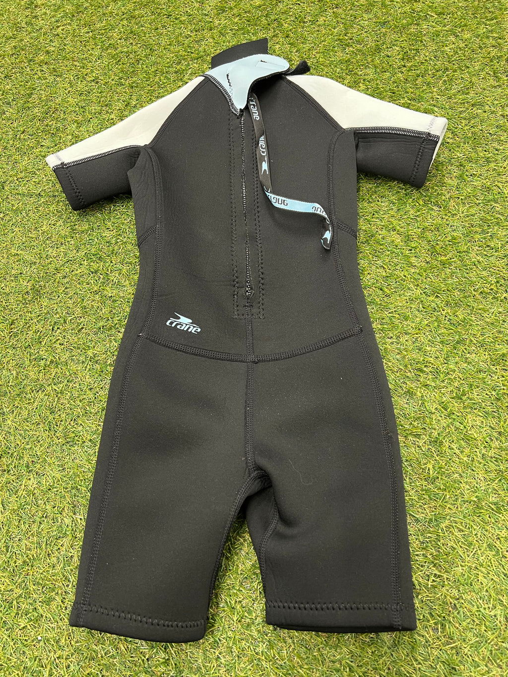 Back view of kids wetsuit showing black colour with back zipper partially open on grassy surface