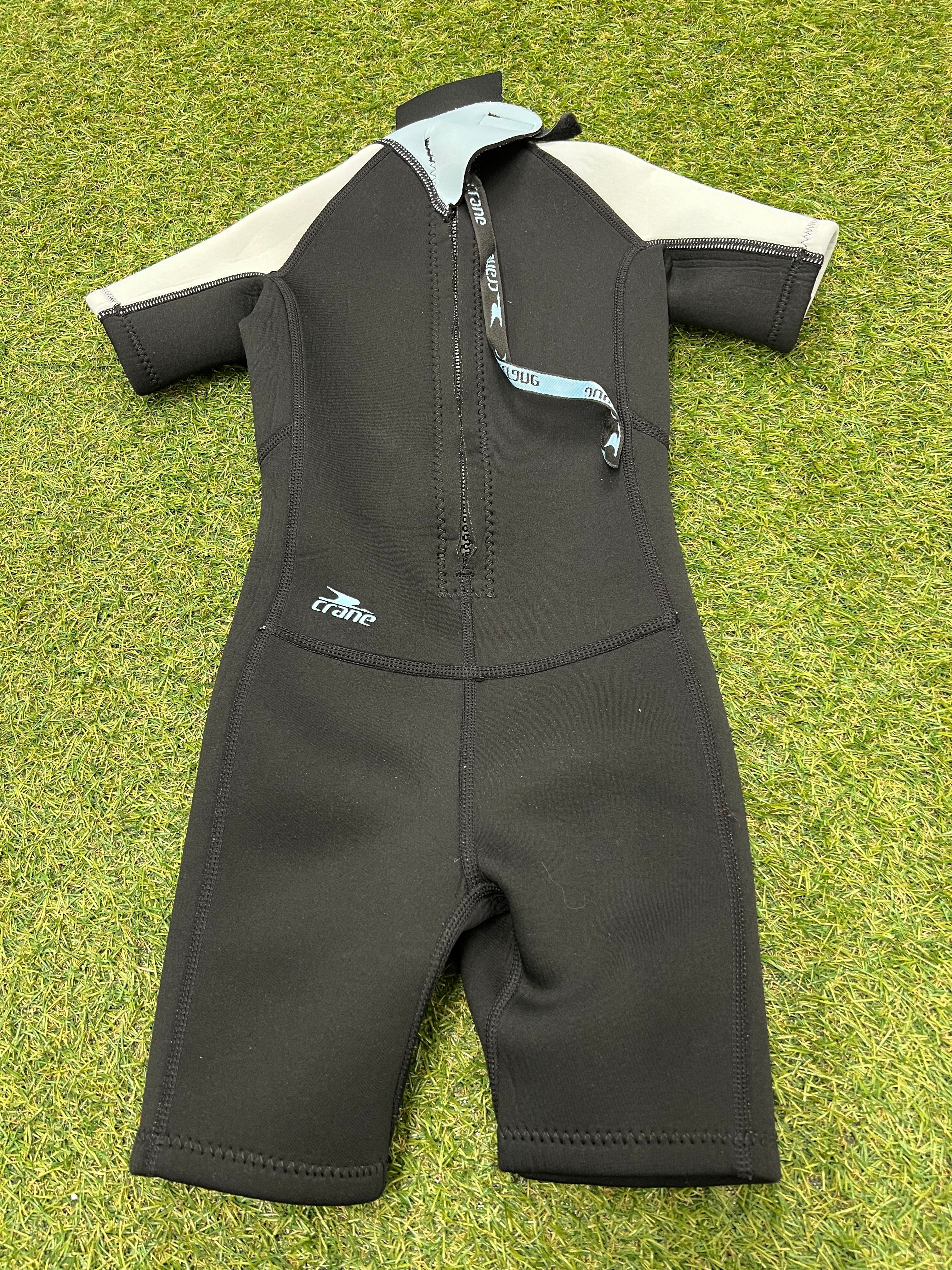 Back view of kids wetsuit showing black colour with back zipper partially open on grassy surface