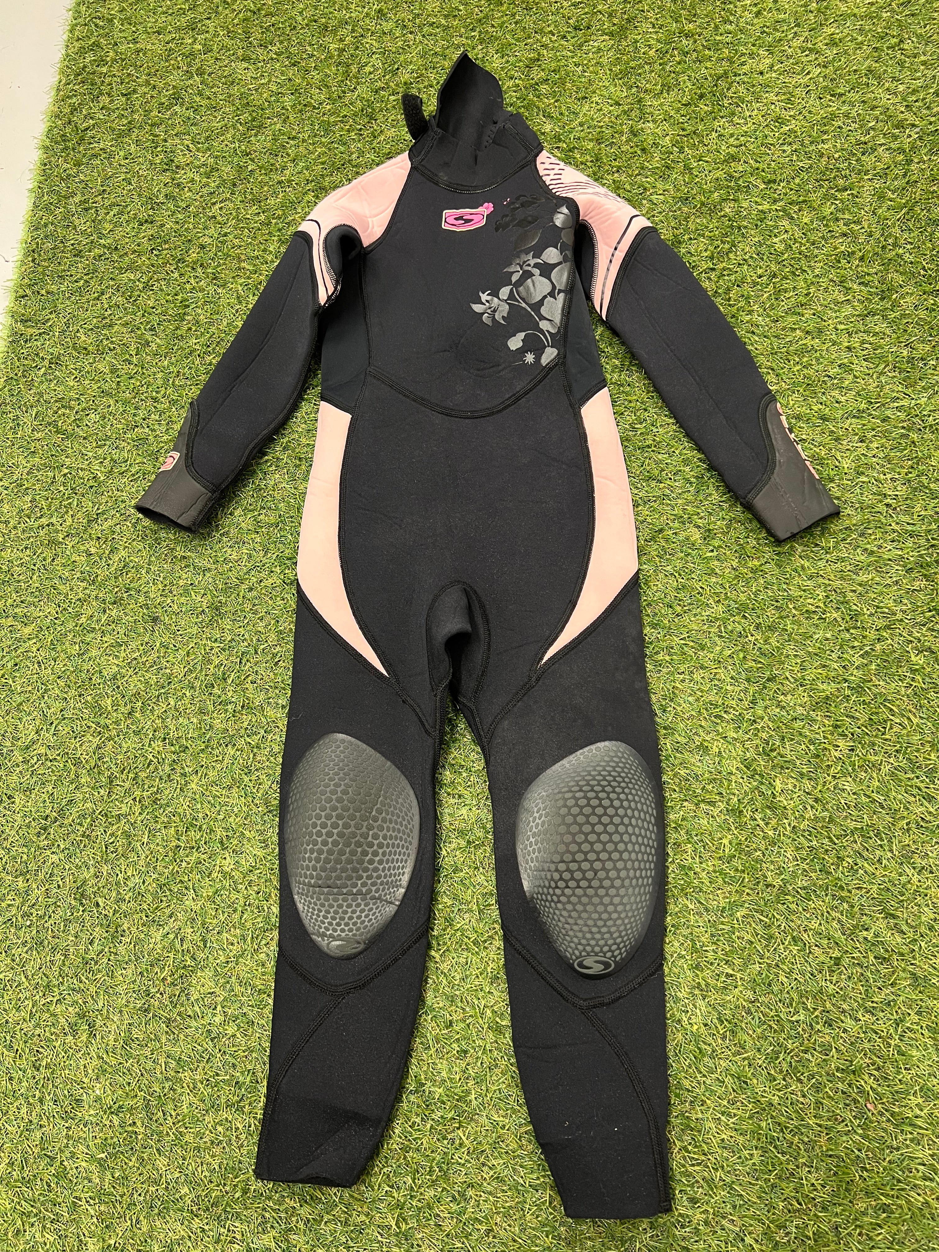 Front view of kids black and pink Sola wetsuit with floral detail and reinforced knee pads on green grass