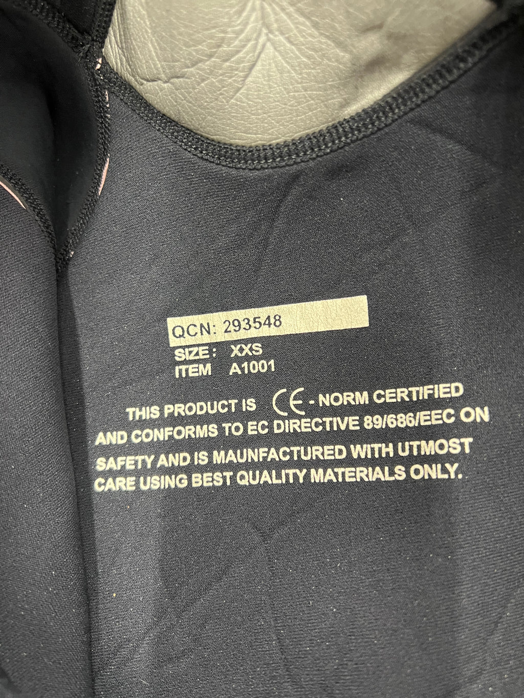 Close-up image of inside wetsuit tag indicating size XXS, CE certification and quality manufacturing text