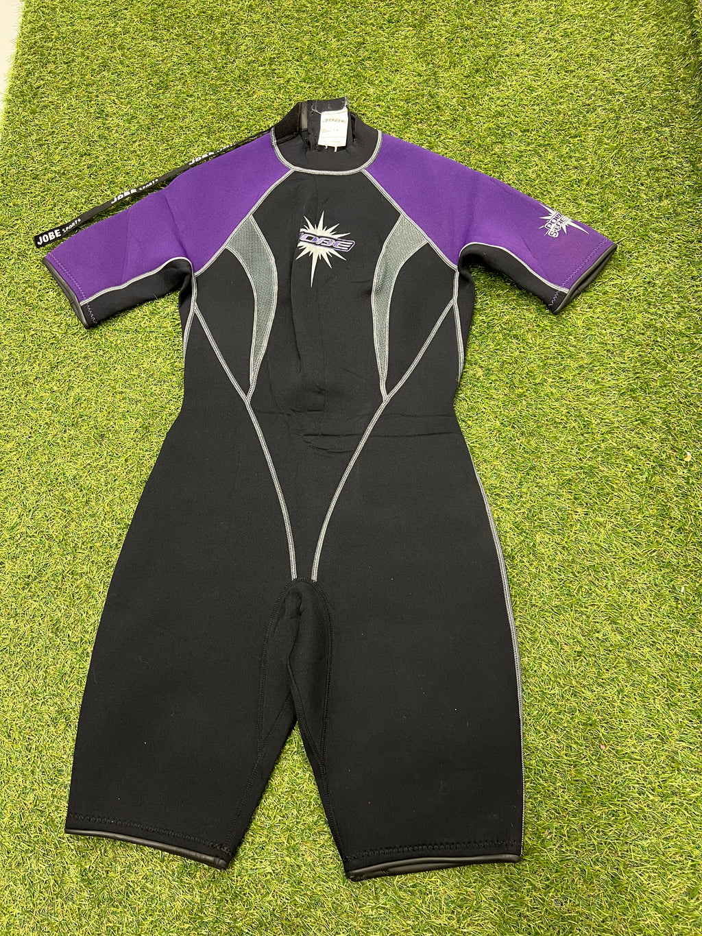 Front view of Jobe kids short sleeve wetsuit in black and purple with white detailing on grass surface