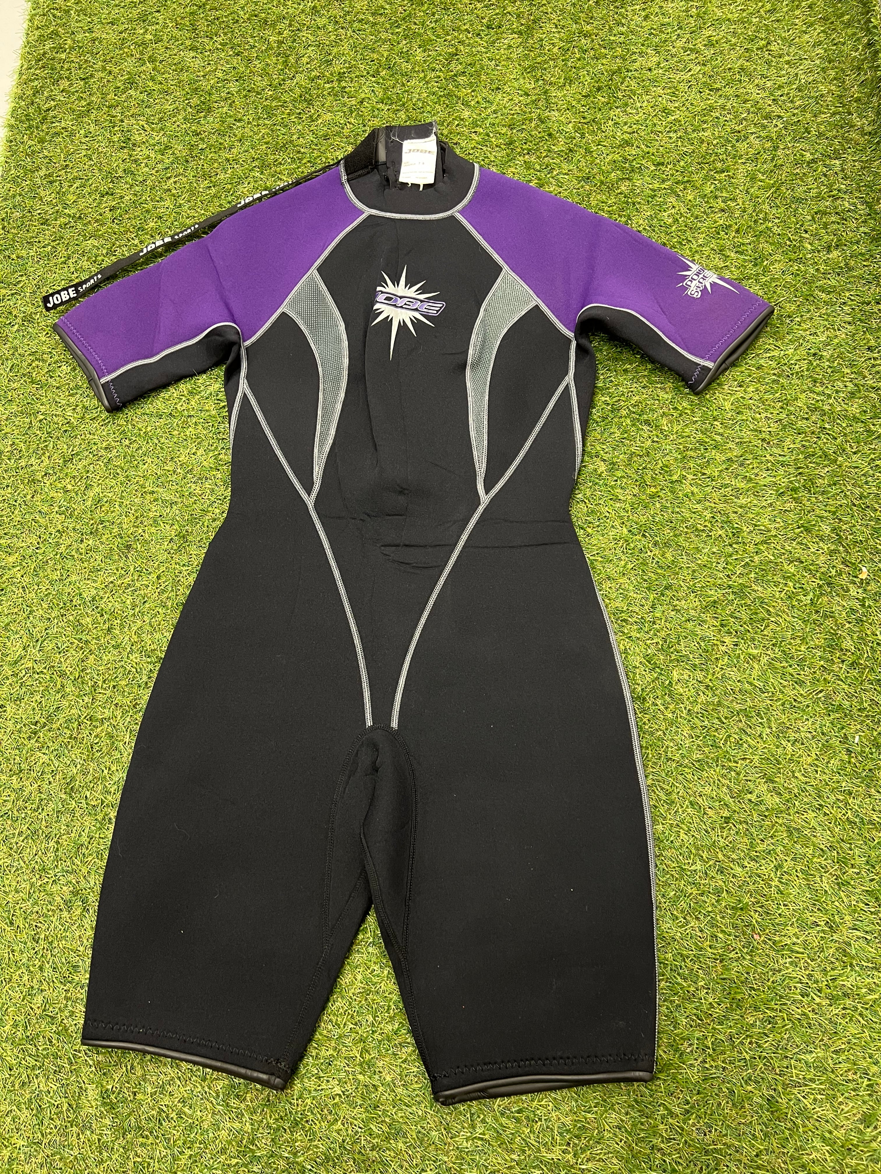 Front view of Jobe kids short sleeve wetsuit in black and purple with white detailing on grass surface