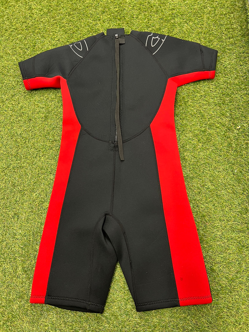 Back view of CIC kids shortie wetsuit showing the rear zip and red side panels on grass