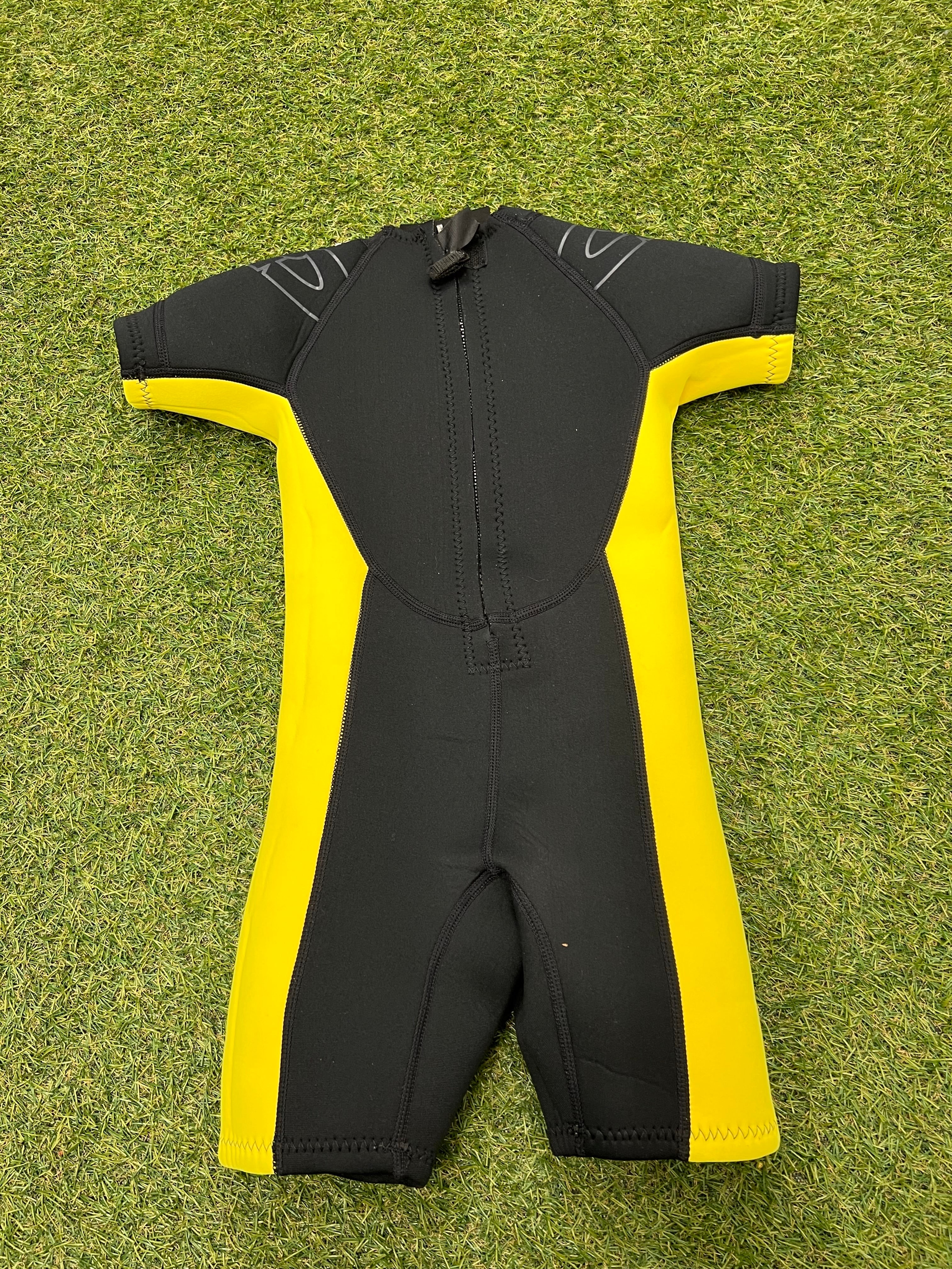 Back view of a kids shortie wetsuit in black and yellow, featuring a back zipper and sturdy stitching detail, laid on grass