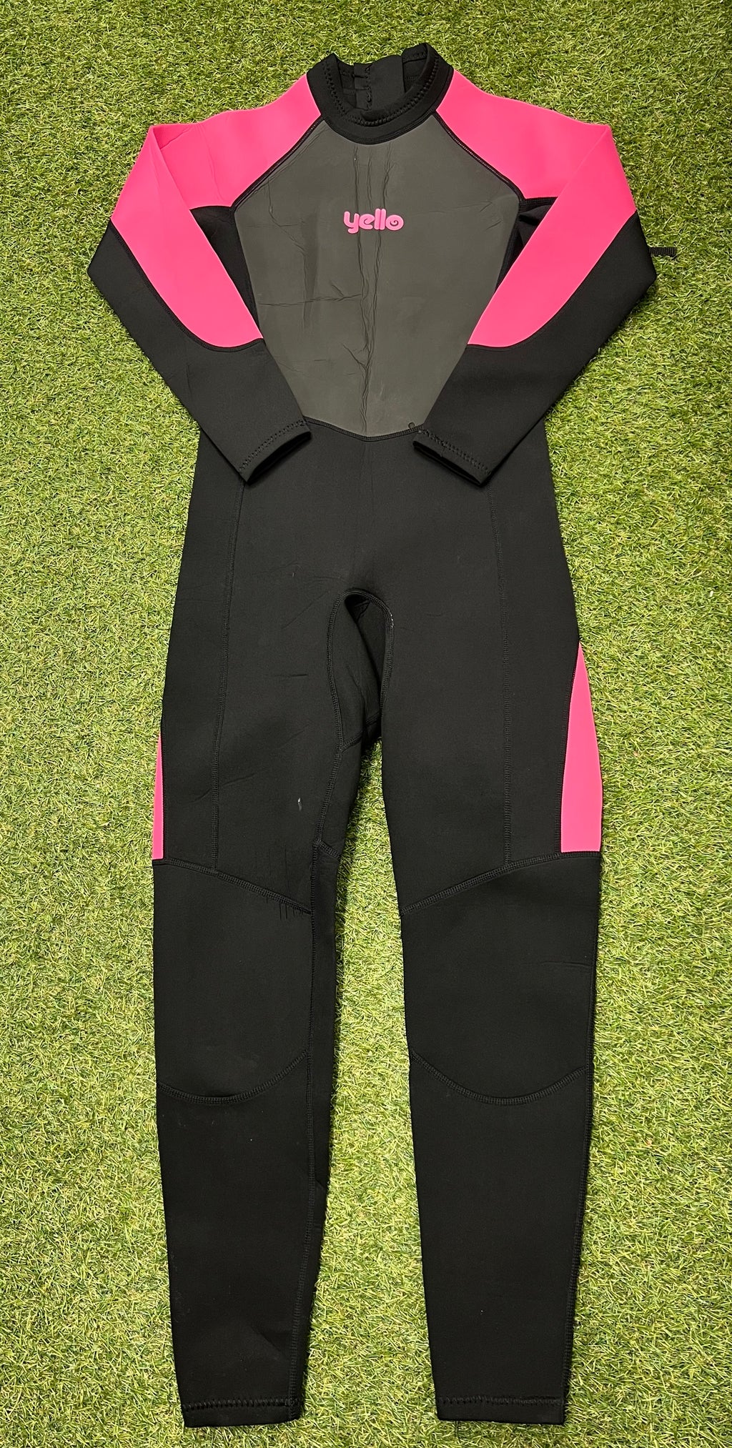 Full length adult wetsuit laid flat on grass with black base and bright pink sleeves and side panels, front view