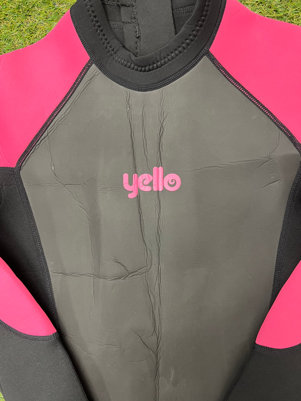 Close-up of the wetsuit chest area showing pink 'yello' logo on grey panel with pink and black sleeves