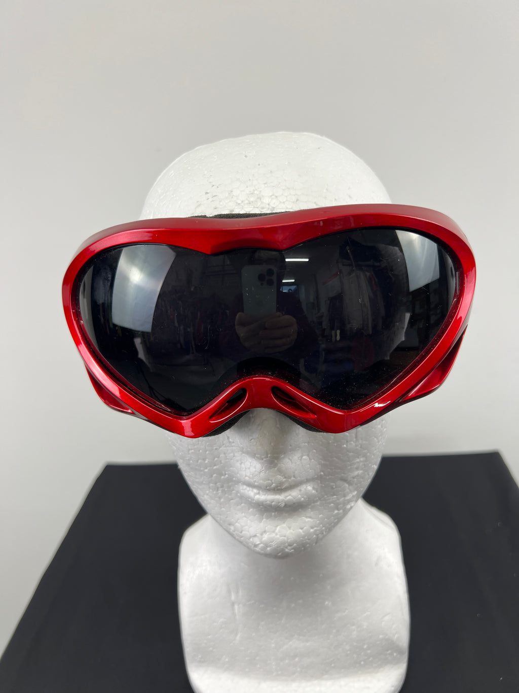Front view of red ski goggles with tinted black lens displayed on a white mannequin head