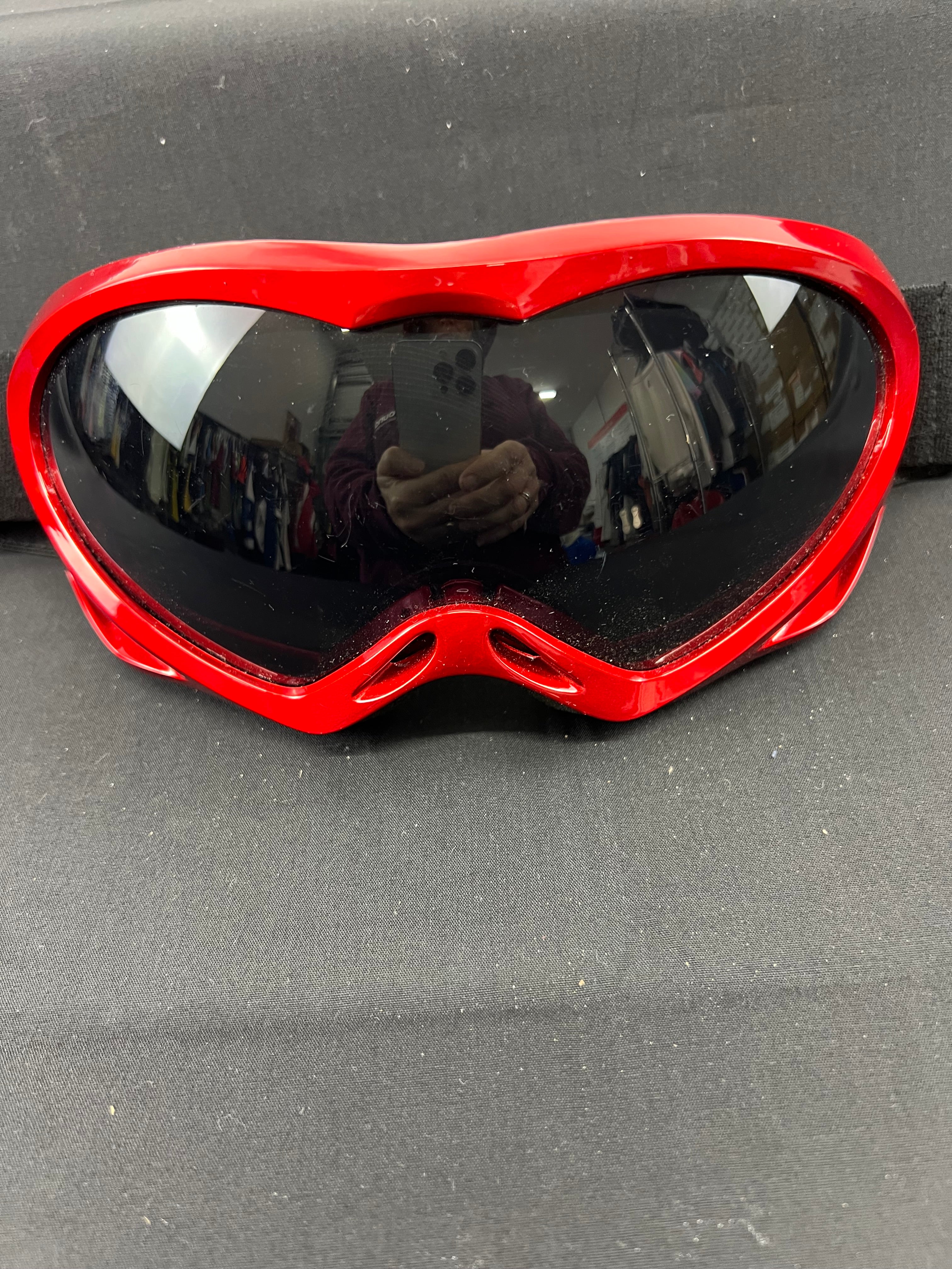 Close-up front view of red ski goggles with dark lens on black surface