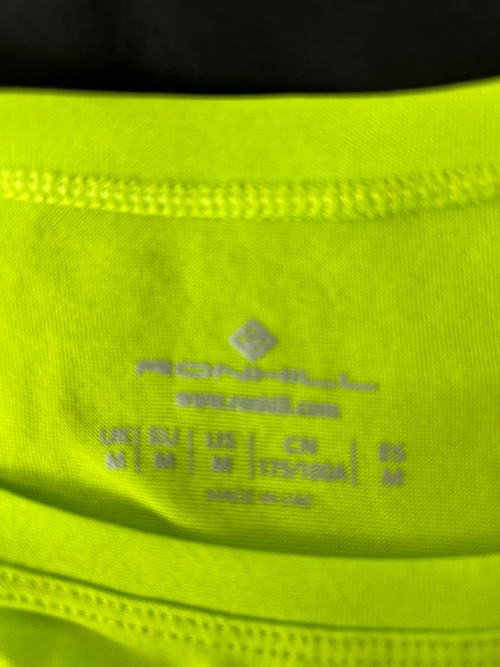 Close-up image of Ronhill brand label and size details inside bright yellow running top