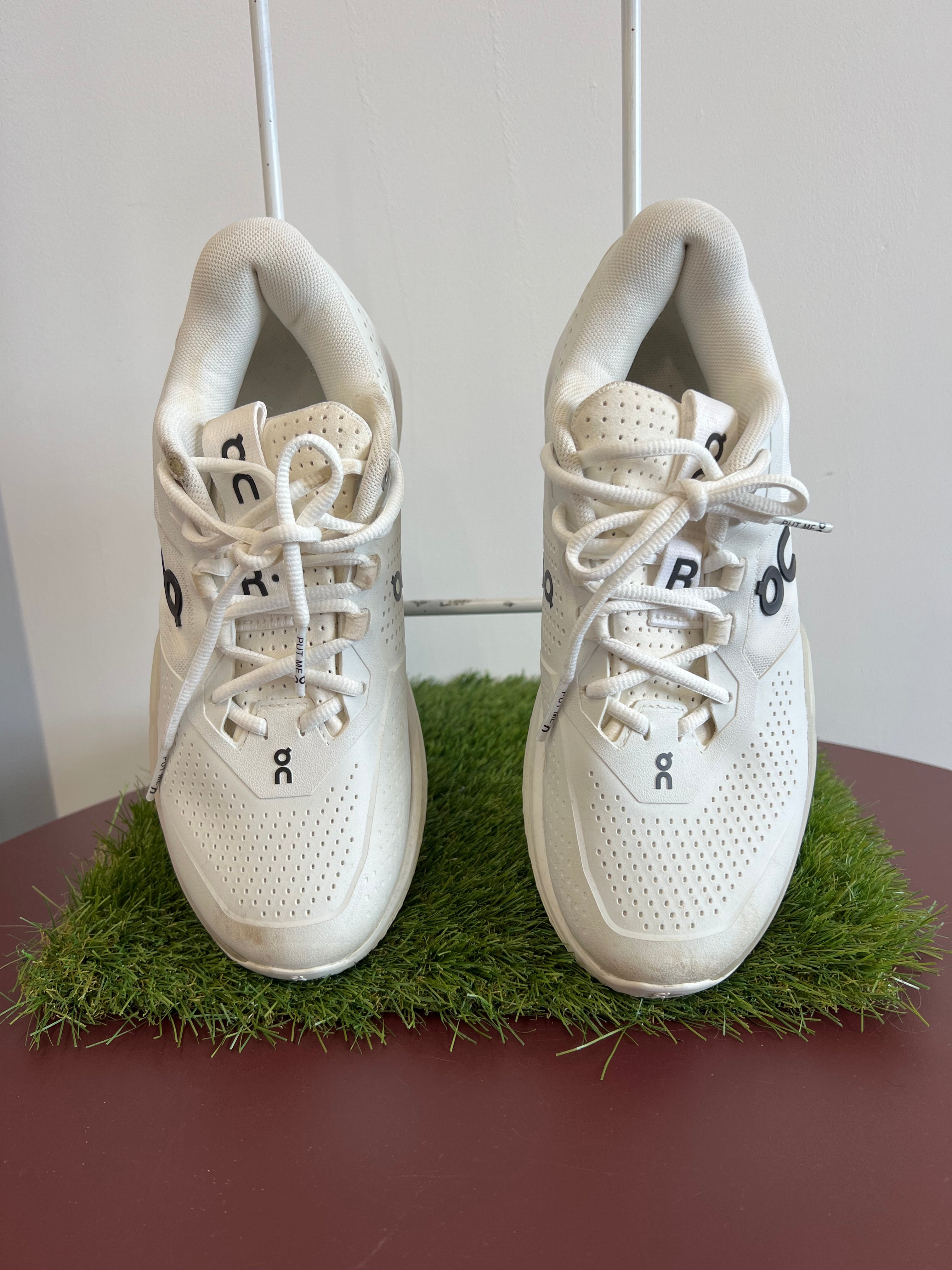 Pair of white perforated trainers with laces viewed from above on artificial grass