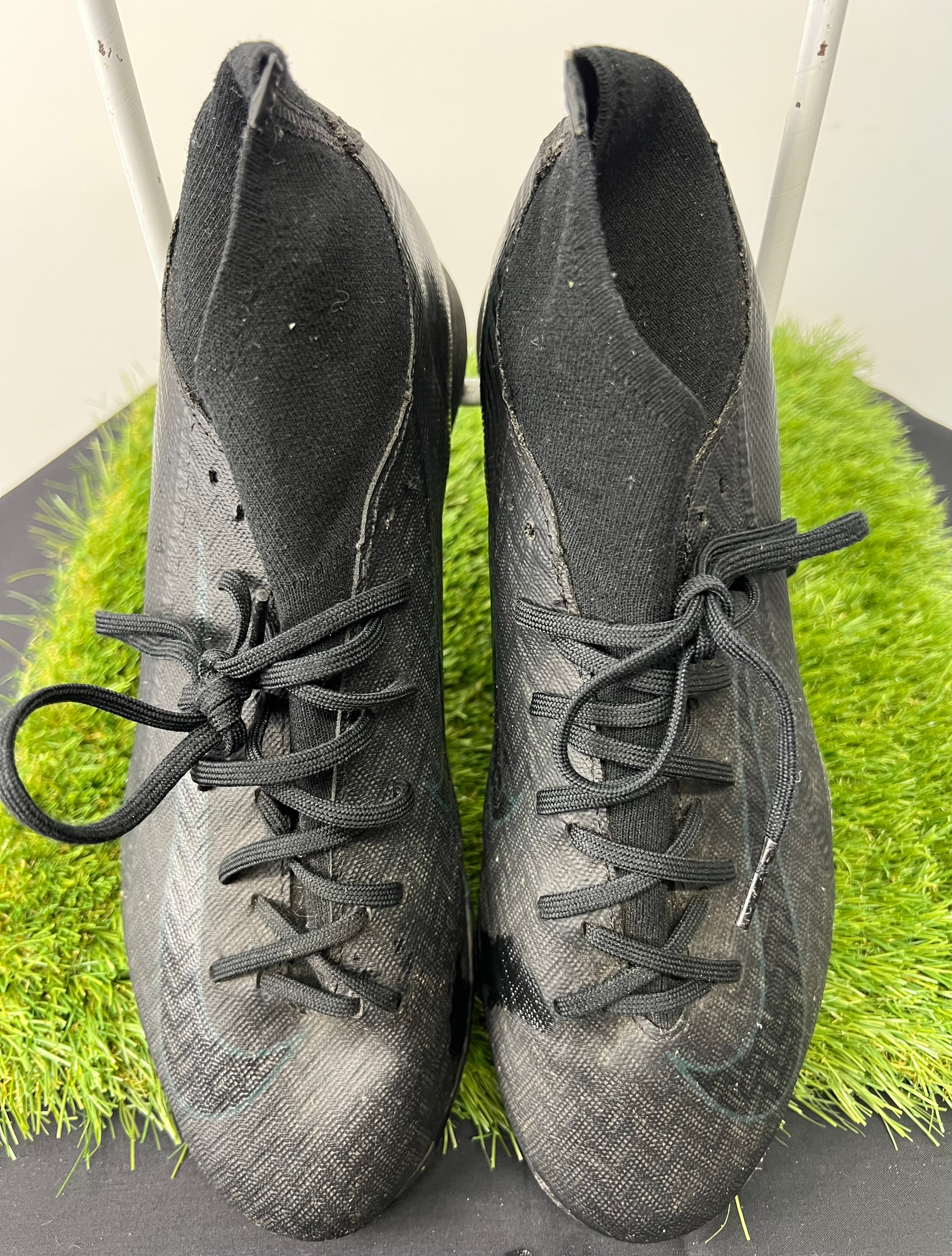 Top view of a pair of black Nike Astro Turf football boots with laces on synthetic grass