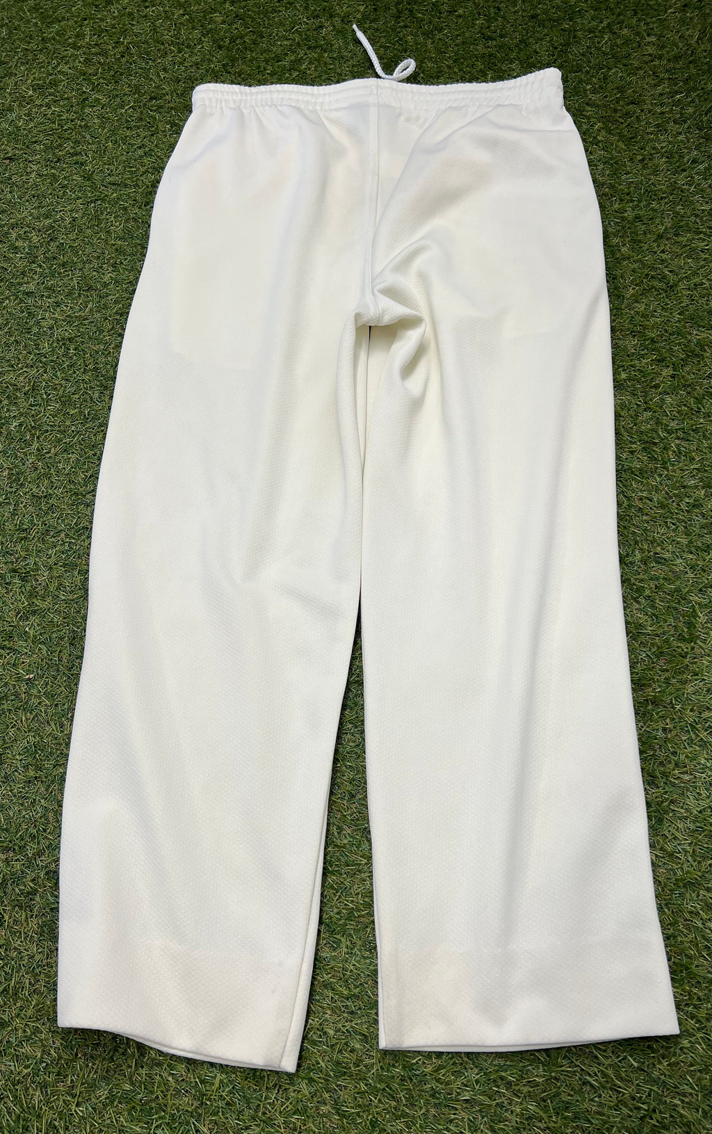 Back view of white Slazenger cricket trousers on grass background