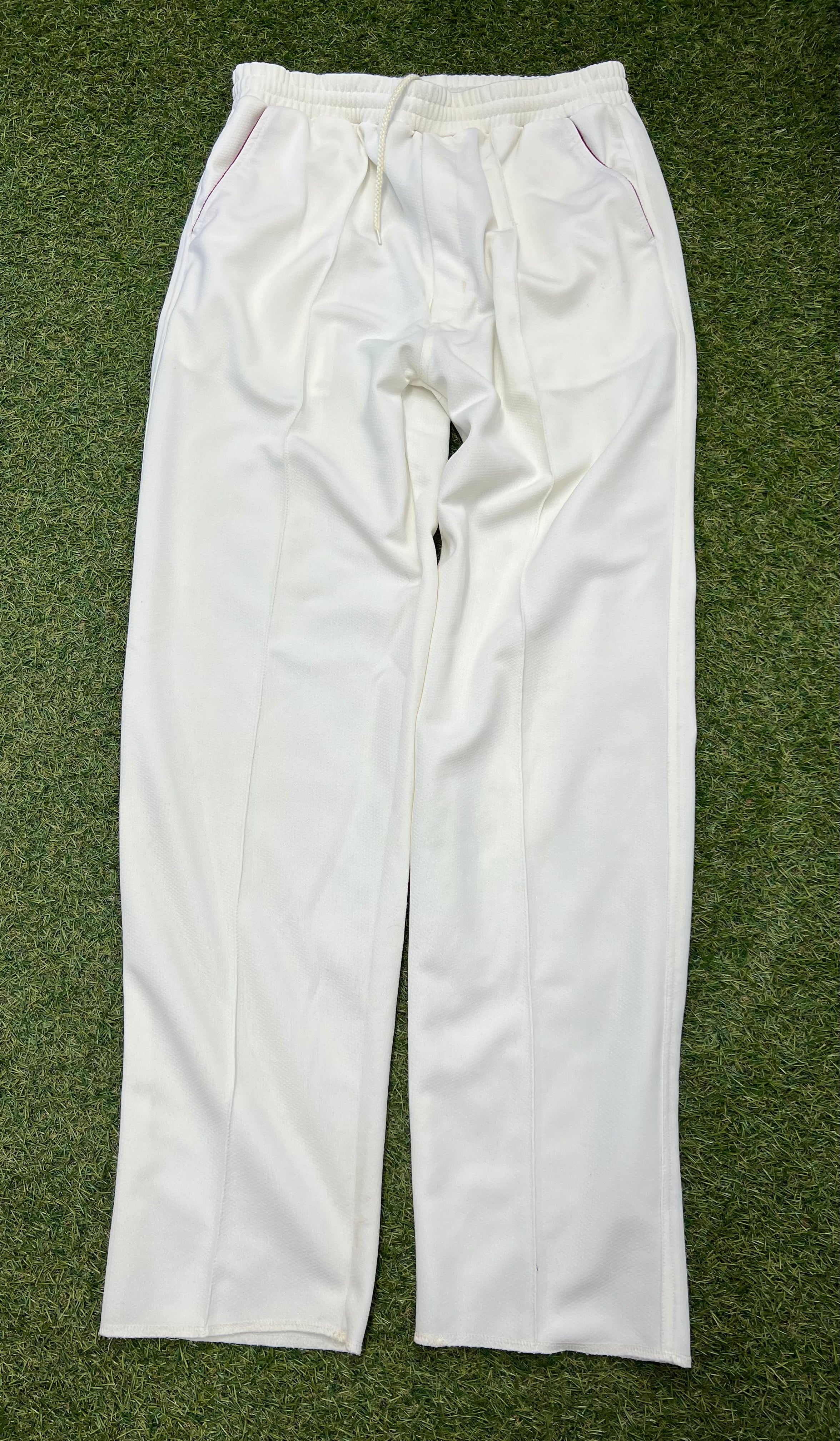 Front view of white Slazenger men’s cricket trousers size small laid flat on grass