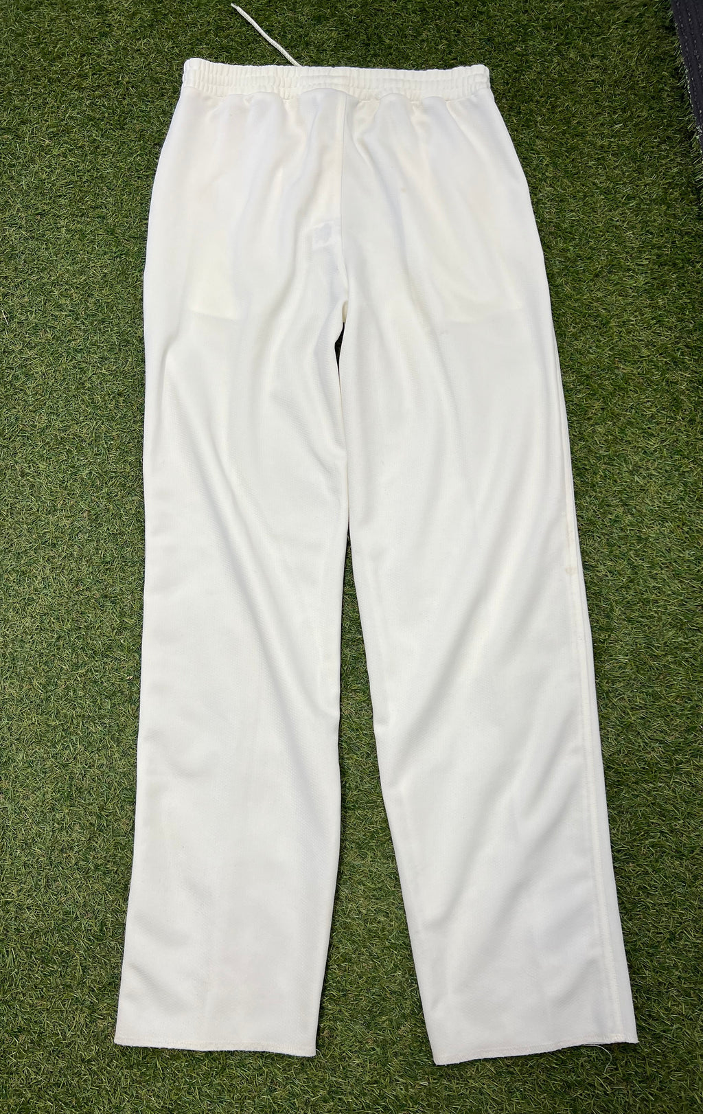 Rear view of white Slazenger men’s cricket trousers size small laid flat on grass