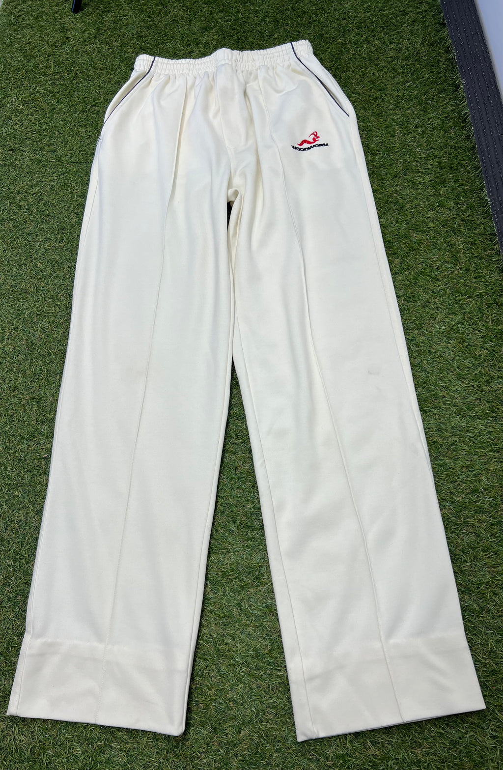 Woodworm men’s cricket trousers laid flat on grass showing full front view