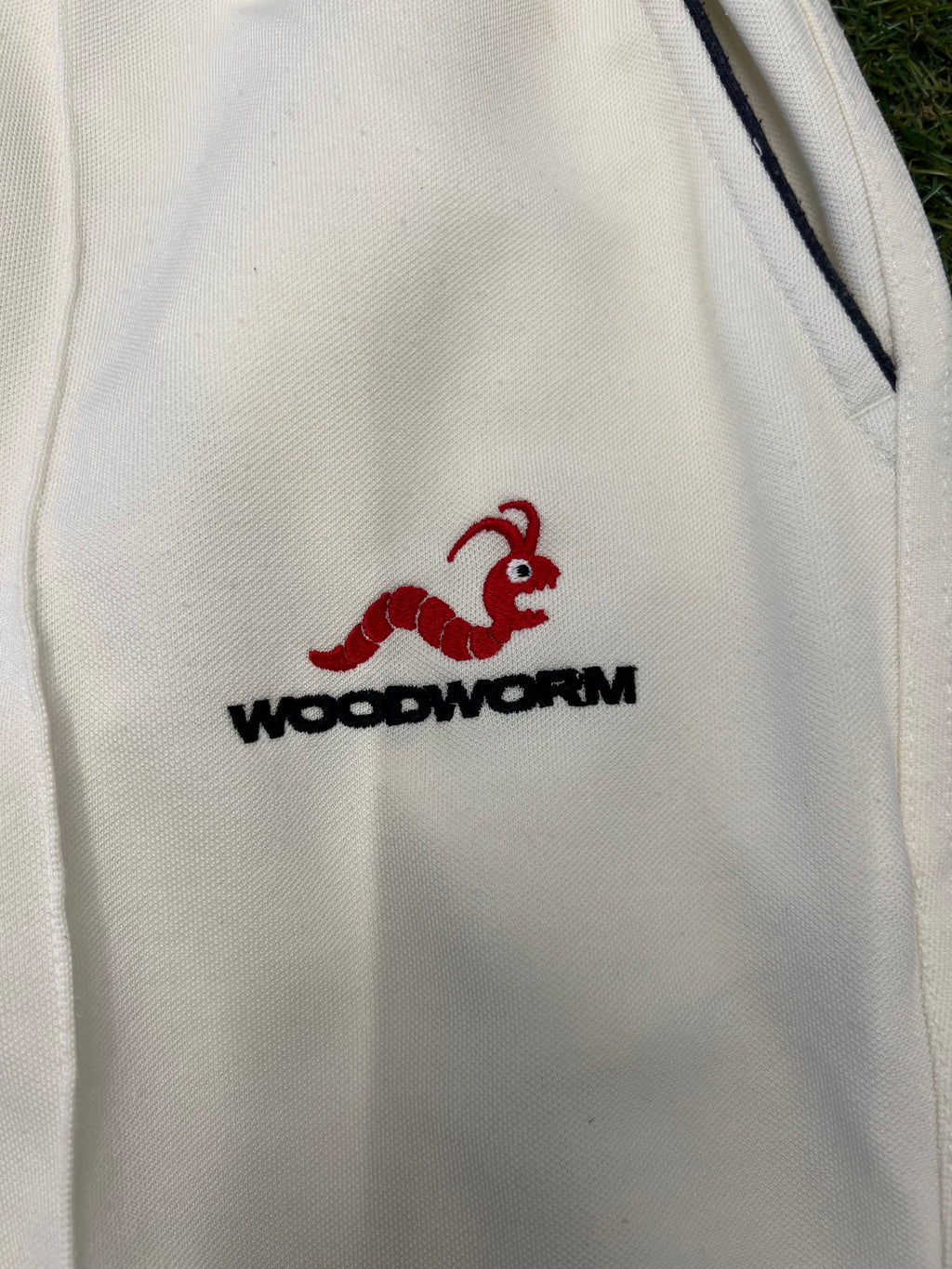 Close-up of Woodworm logo embroidered in red and black on white cricket trousers