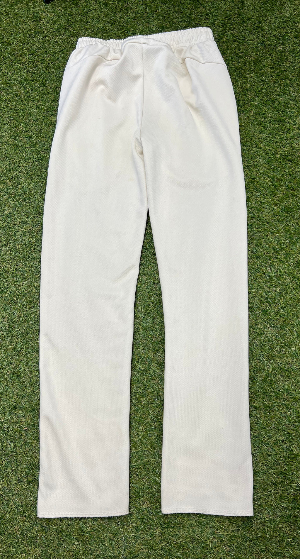 Back view of Slazenger kids white cricket trousers laid flat on grass