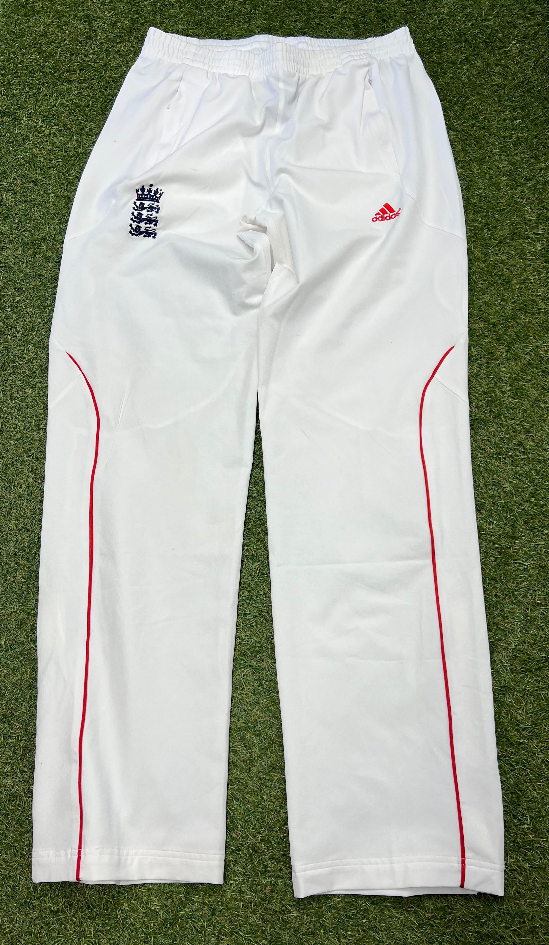 Front view of men's white Adidas cricket trousers with elastic waistband and red piping on legs