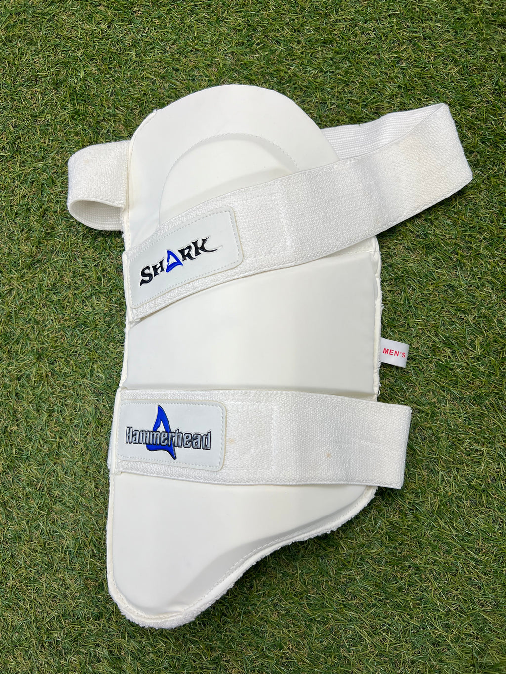 Men’s Shark Hammerhead left-hand thigh pad showing white padded exterior with two velcro straps on grass