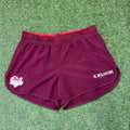 Front view of maroon Kukri Team England women's lightweight sports shorts with red mesh waistband on grass surface