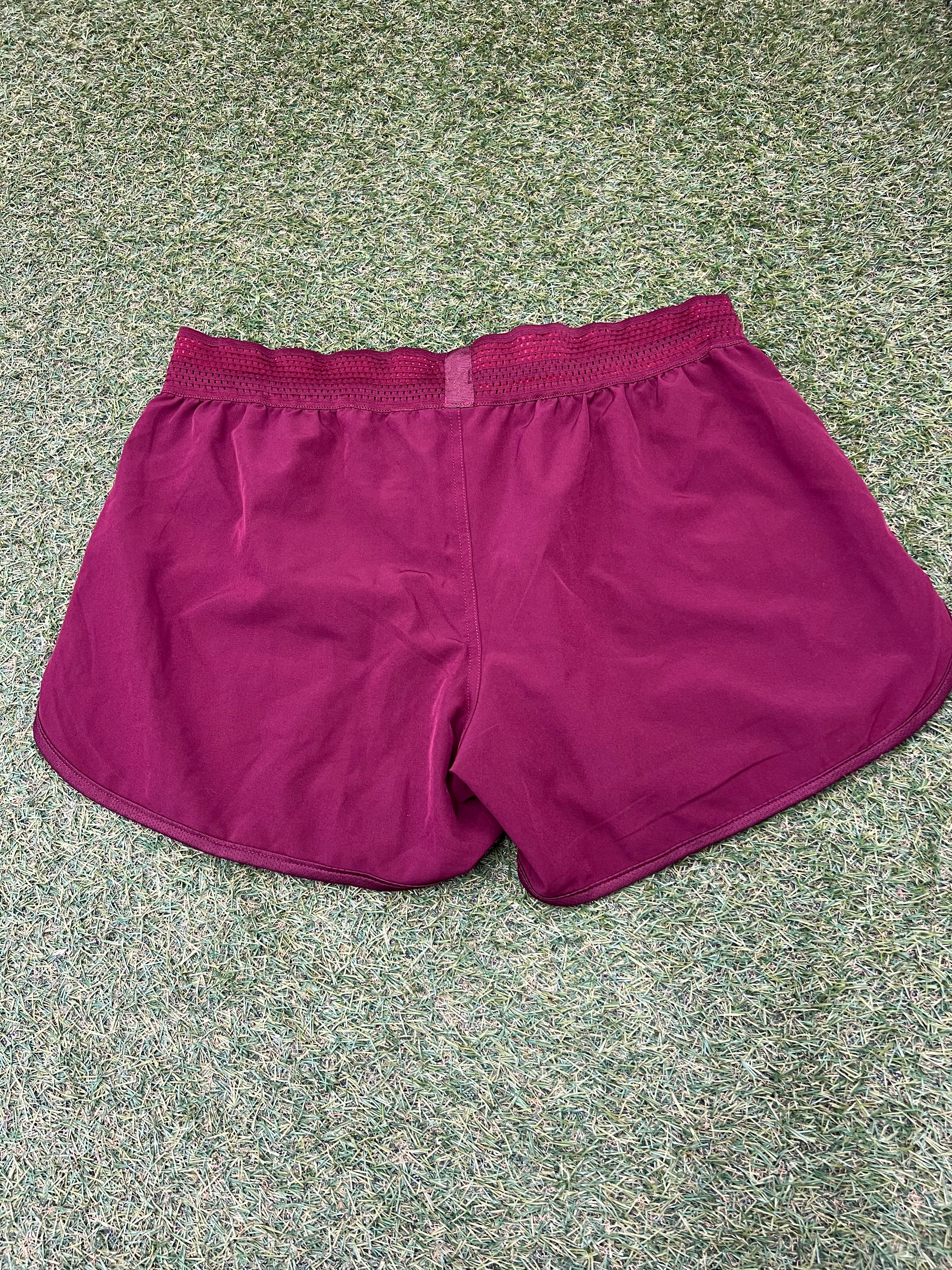 Back view of maroon Kukri Team England women's lightweight sports shorts with red mesh waistband on grass surface