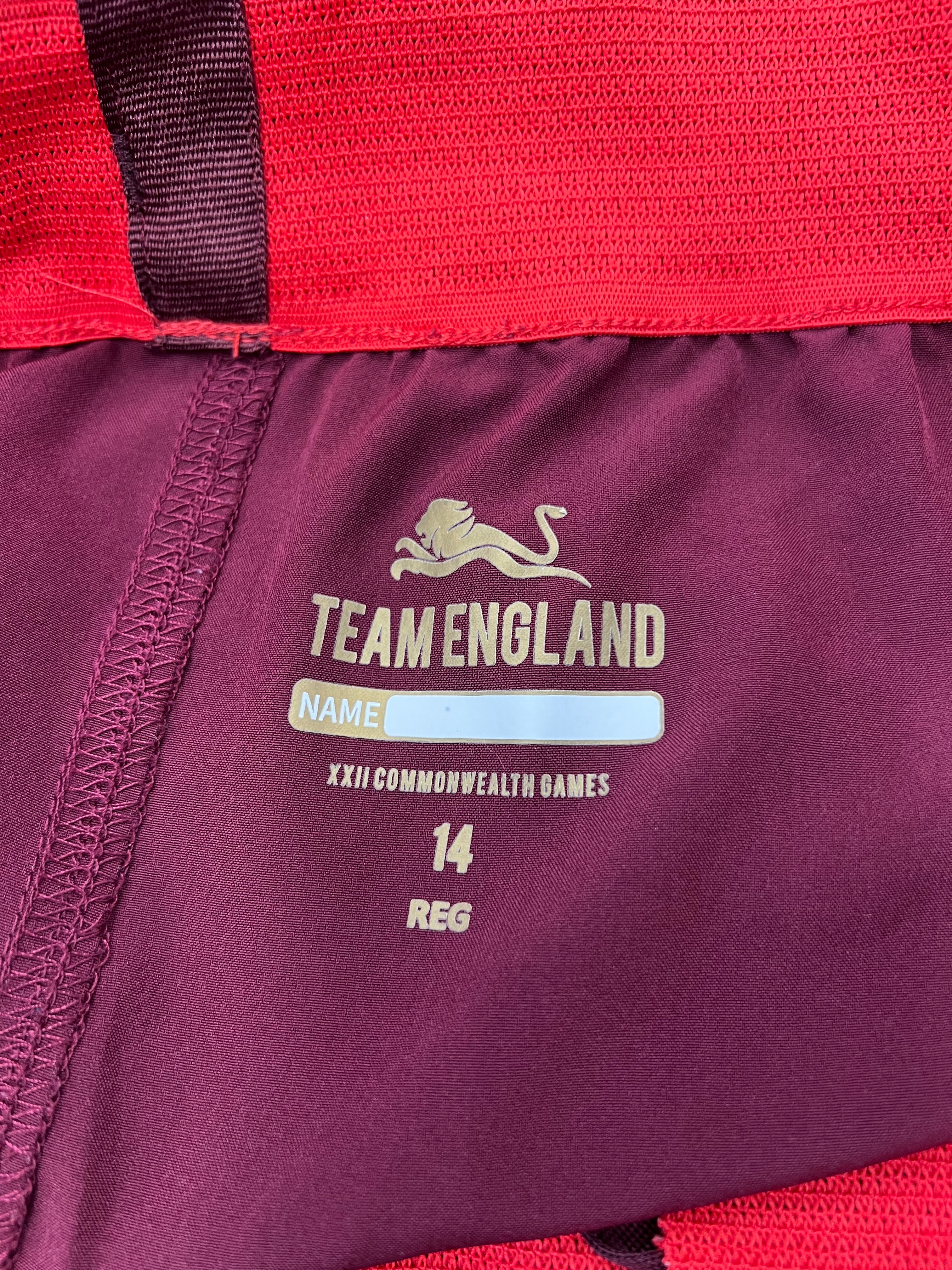 Close-up inside label of Kukri Team England shorts showing name space, XXII Commonwealth Games logo, size 14, and red mesh waistband