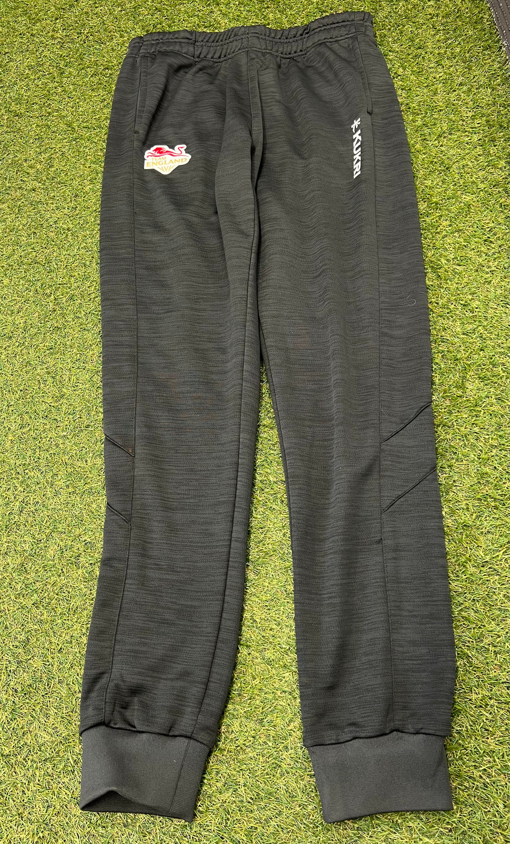 Front view of dark grey Kukri Team England women's tracksuit bottoms with logo and elastic waistband on grass