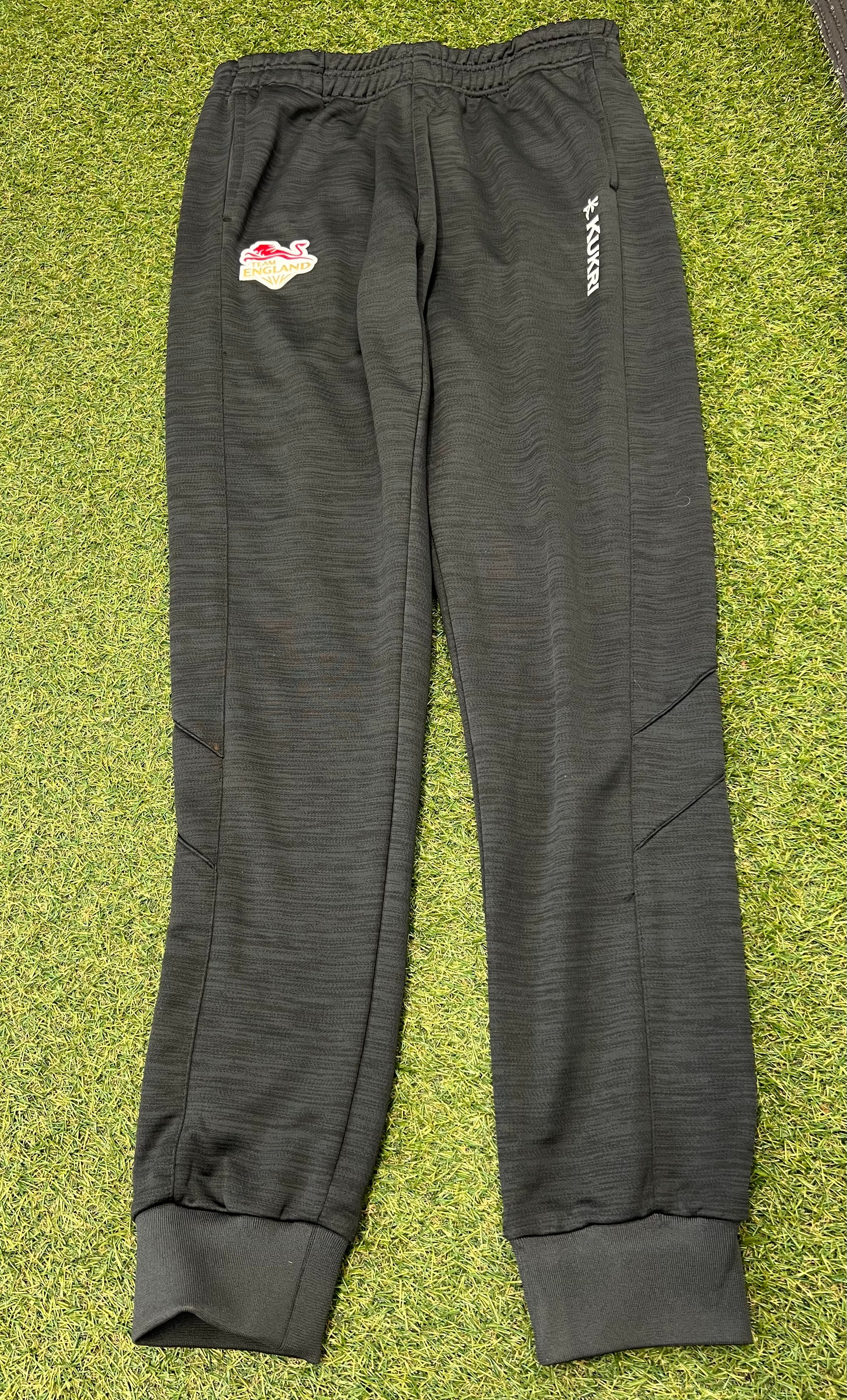 Front view of dark grey Kukri Team England women's tracksuit bottoms with logo and elastic waistband on grass