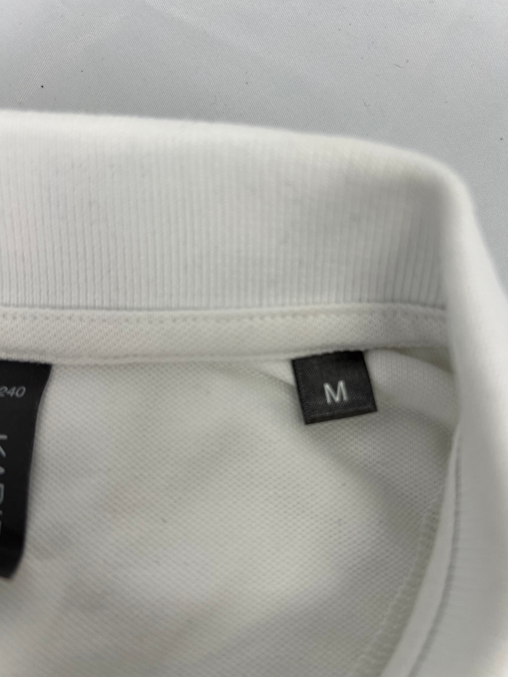 Close-up of collar and size tag marked medium on women’s white polo shirt