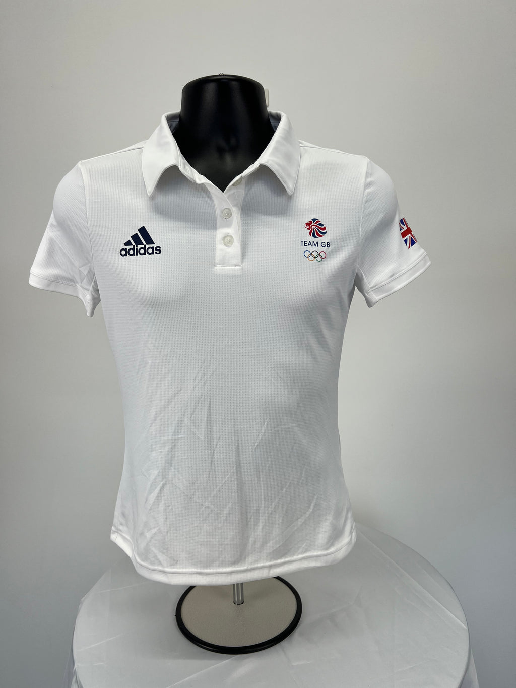 Front view of white women’s Adidas Team GB polo top with logos and button collar