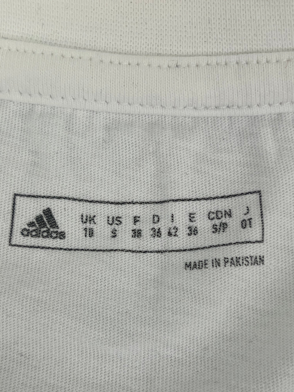Inside neck label showing Adidas sizing and made in Pakistan on white women's T-shirt