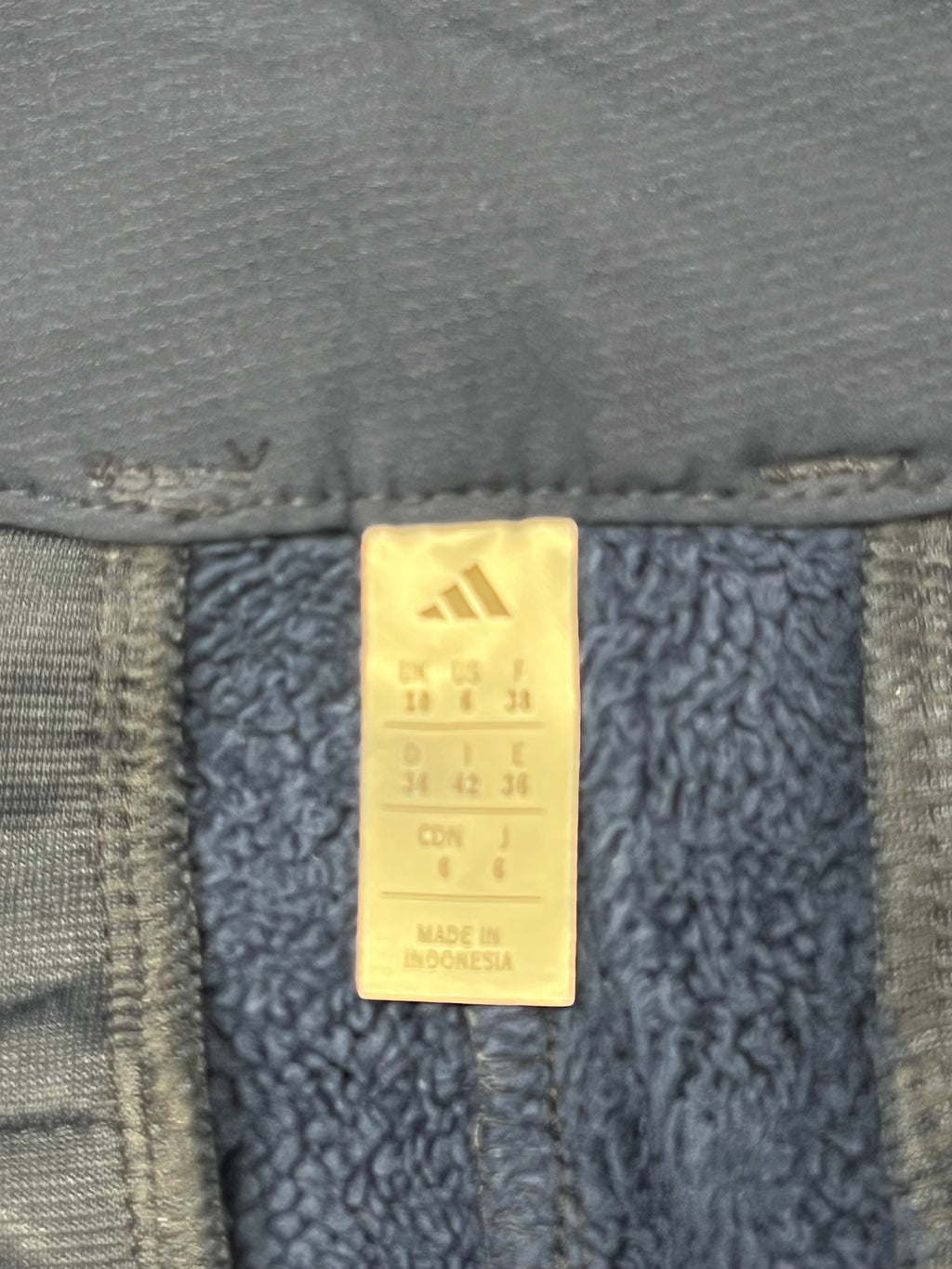 Close-up of Adidas tag inside navy fleece-lined trousers showing sizes and quality