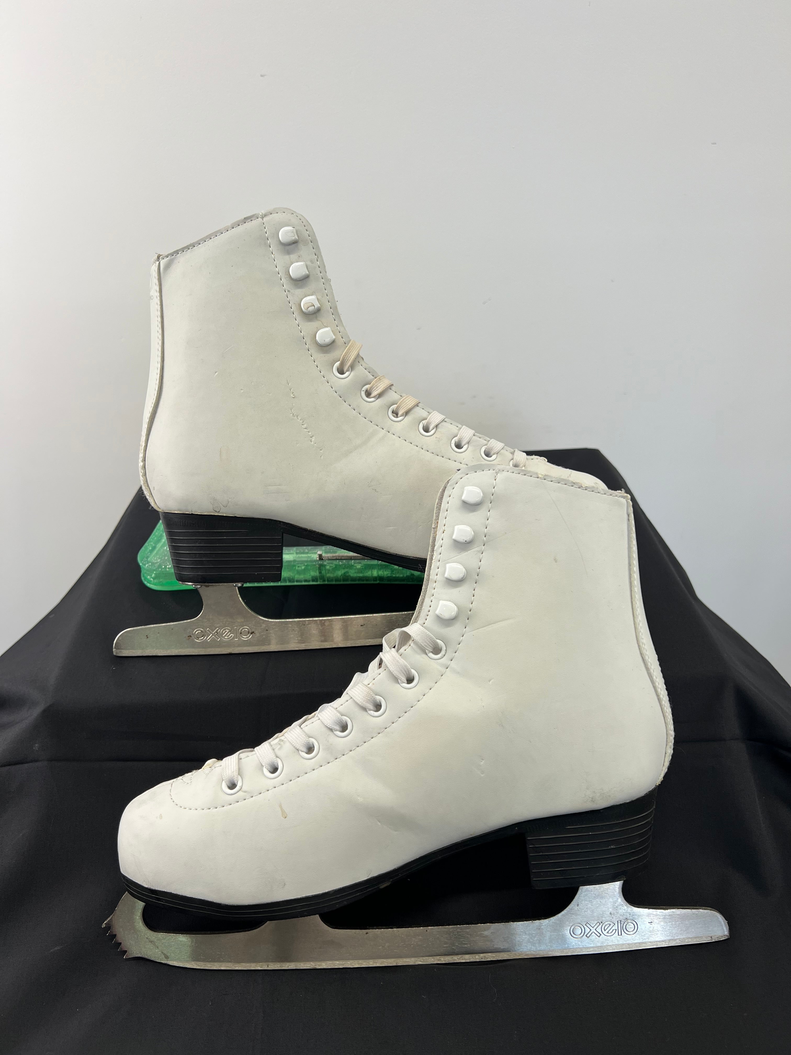 Profile view of white Oxelo figure skates with black heel and durable synthetic leather