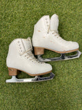 Pair of women’s white leather figure skates with stacked brown heels and chrome Aspire XP blades on grass