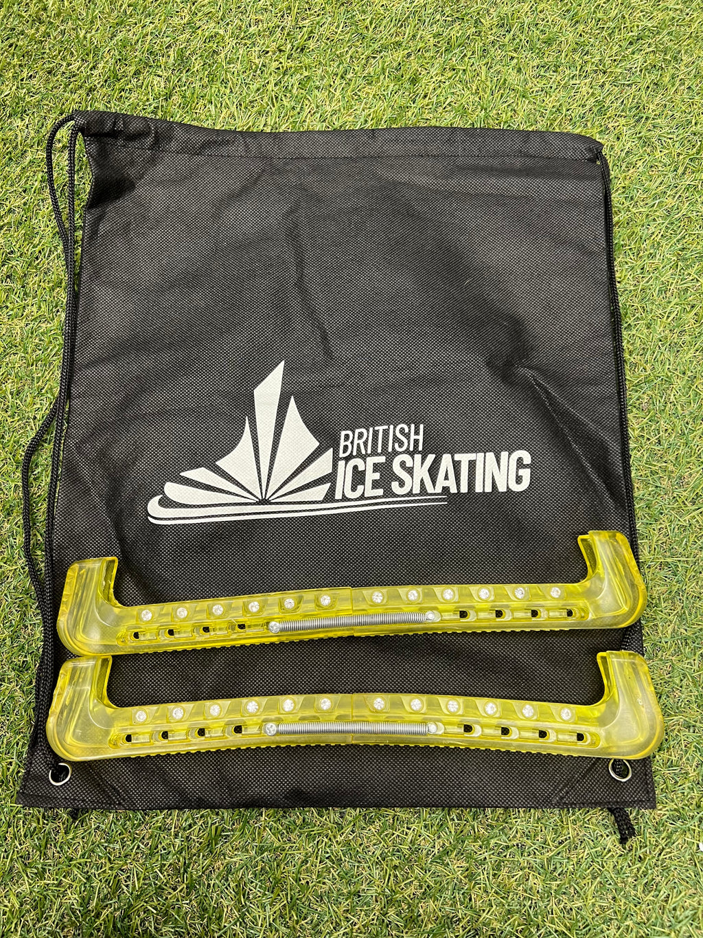 British Ice Skating branded black drawstring bag with yellow protective blade guards on grass
